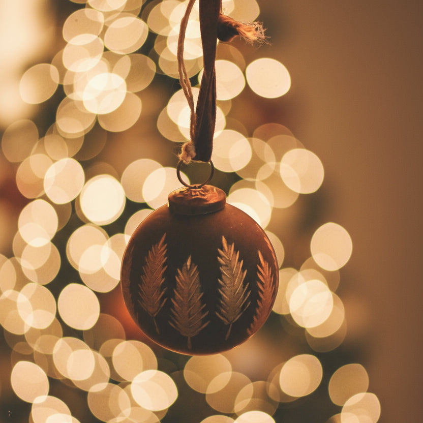 Round bauble ornament with embossed tree design on a background with blurry festive lights