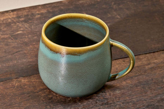 Teal blue Kalini mug from Nkuku with gold rim on a wooden surface