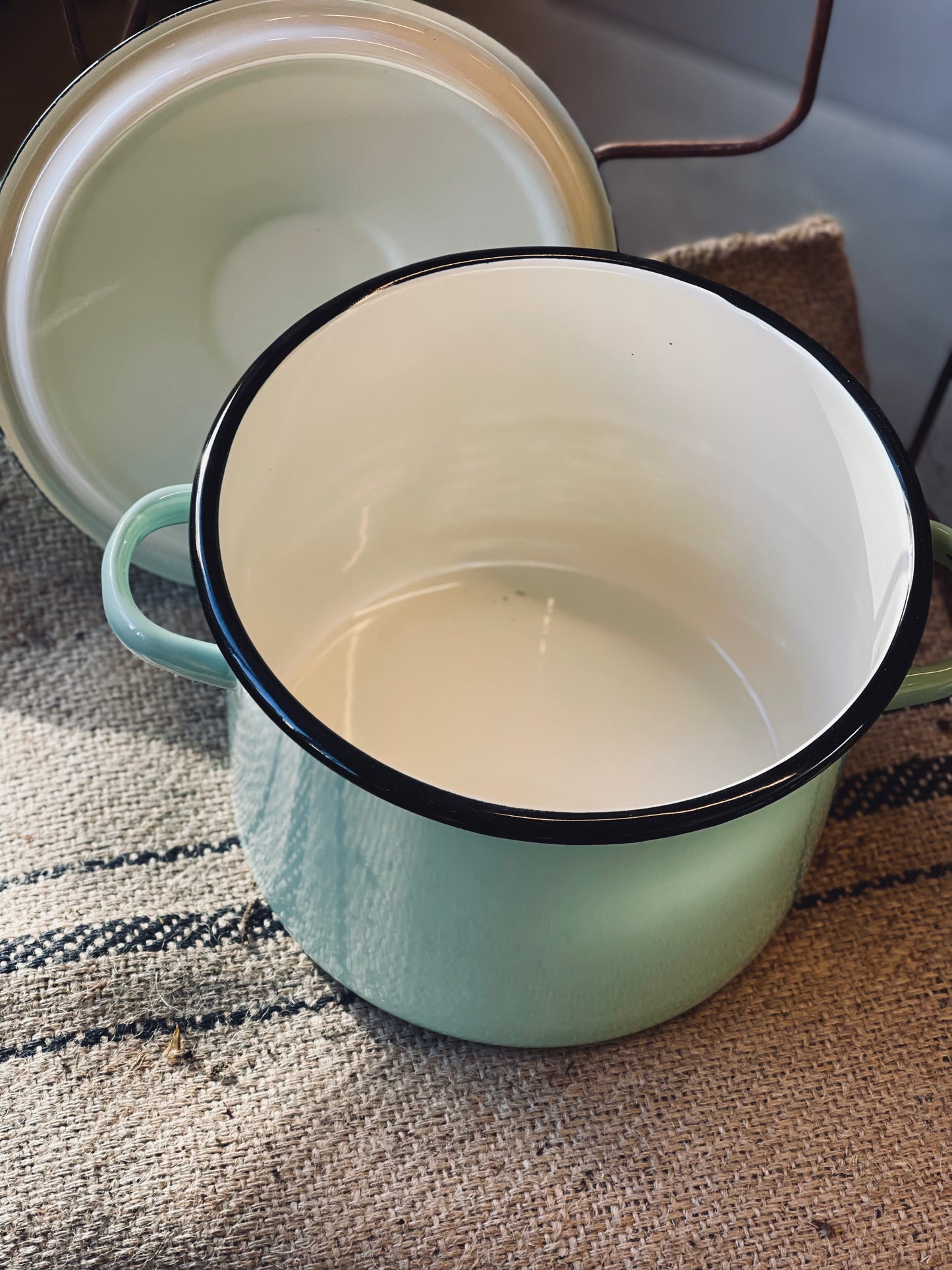Light green enamel pot with black rim on a textured surface
