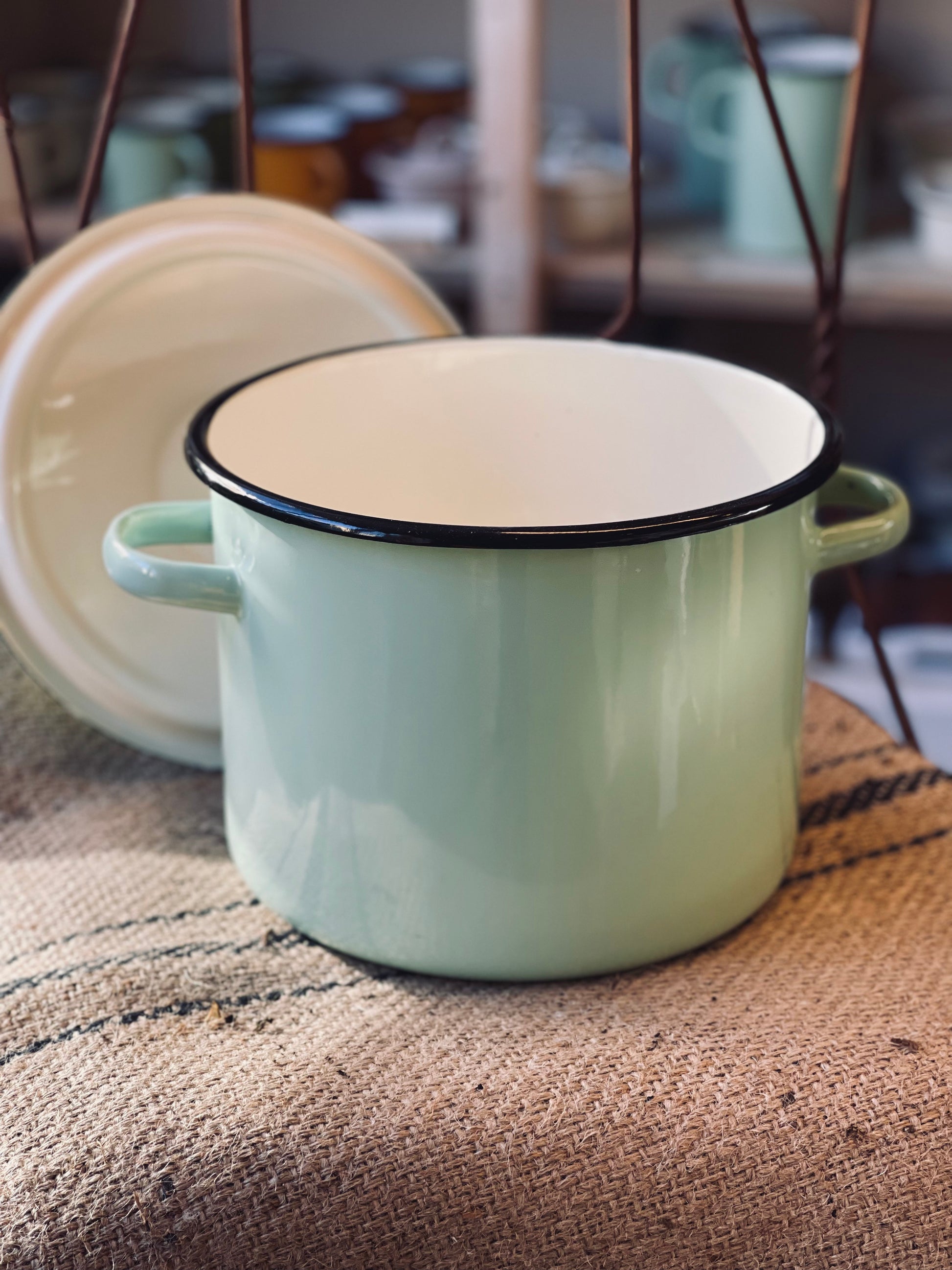 Light green enamel pot with black rim on a textured surface