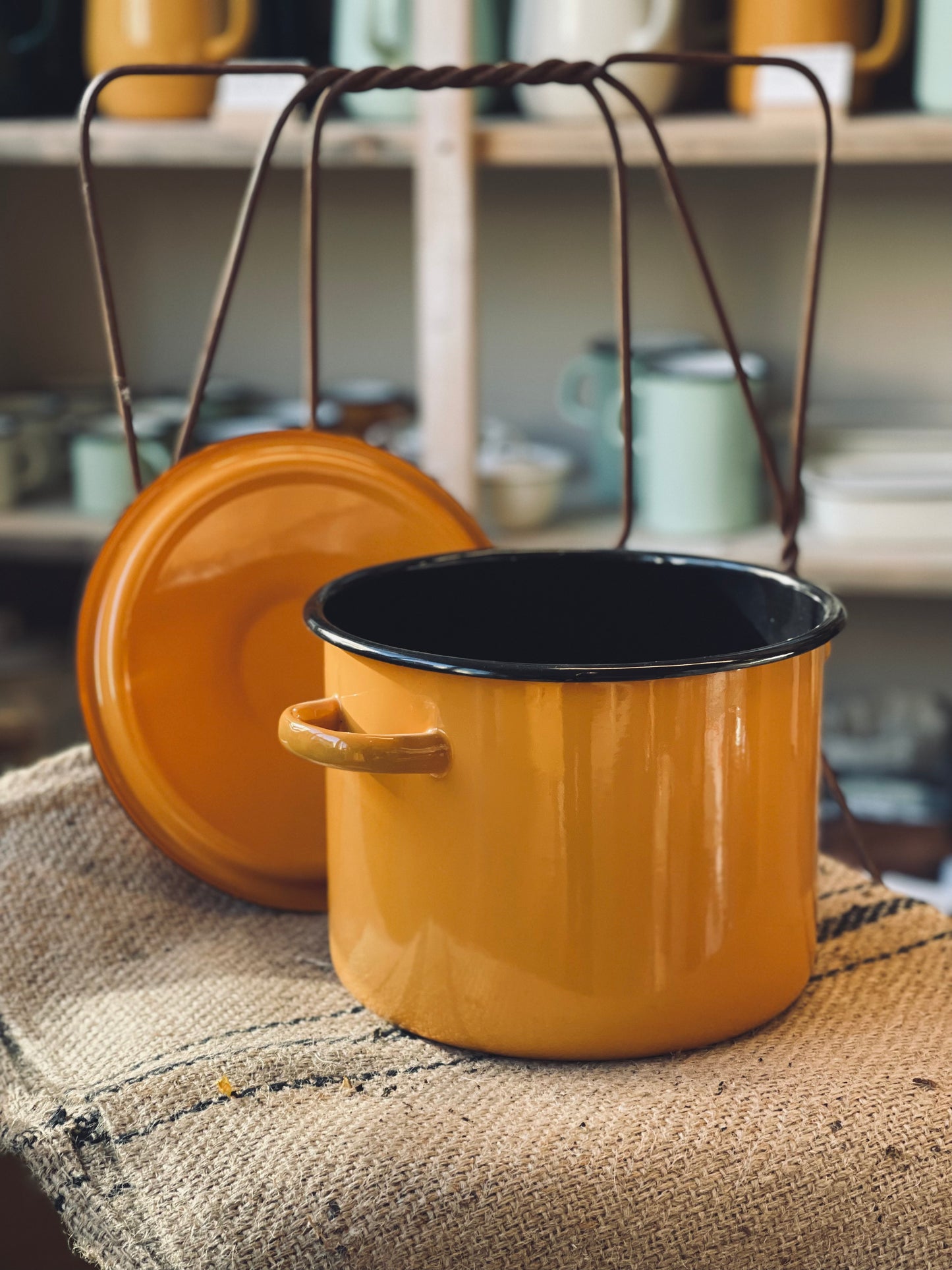 Yellow enameled pot with black interior on a textured surface, with a blurred background of kitchen items.