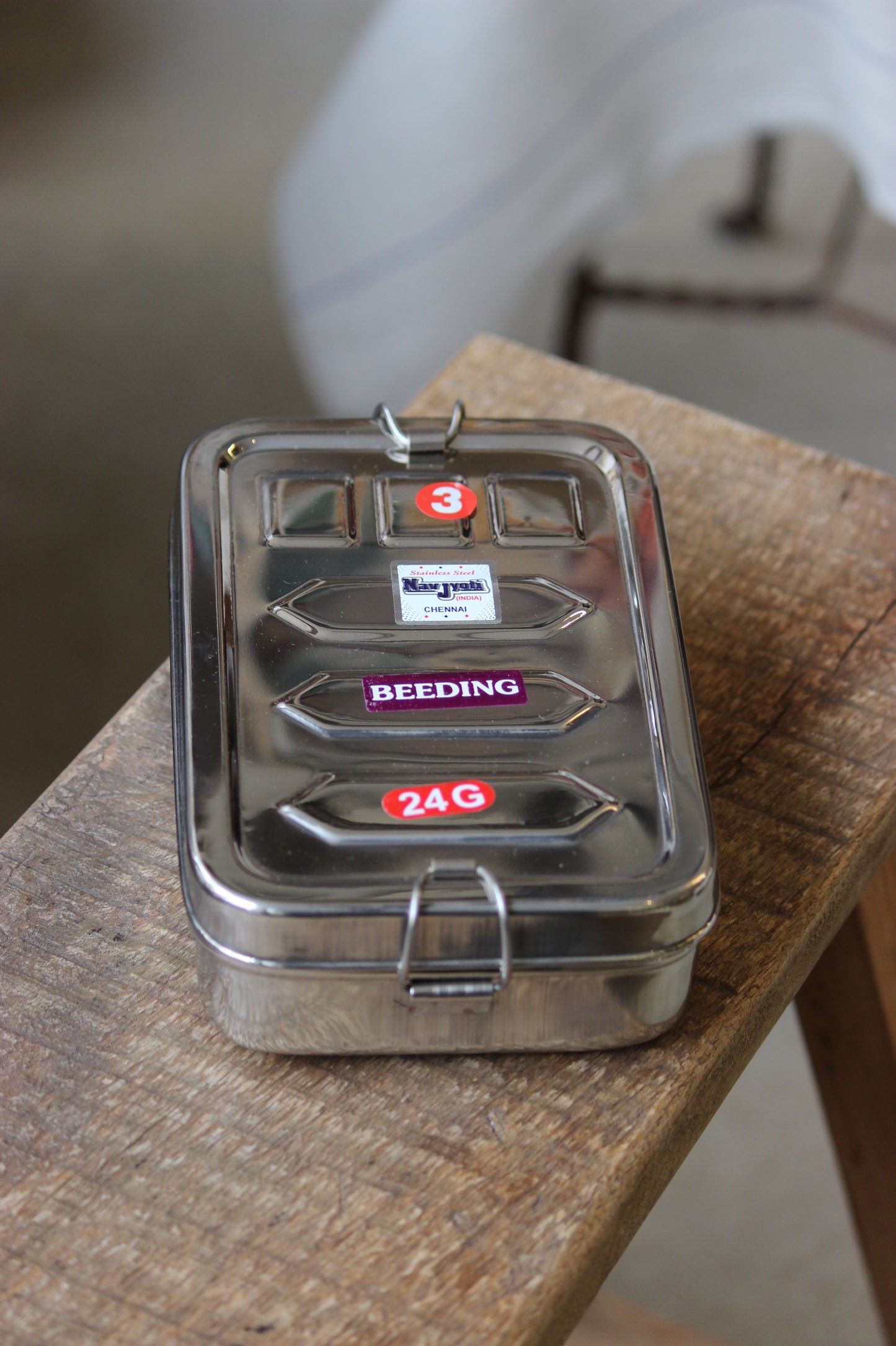 Metallic container with labeled compartments on a wooden surface