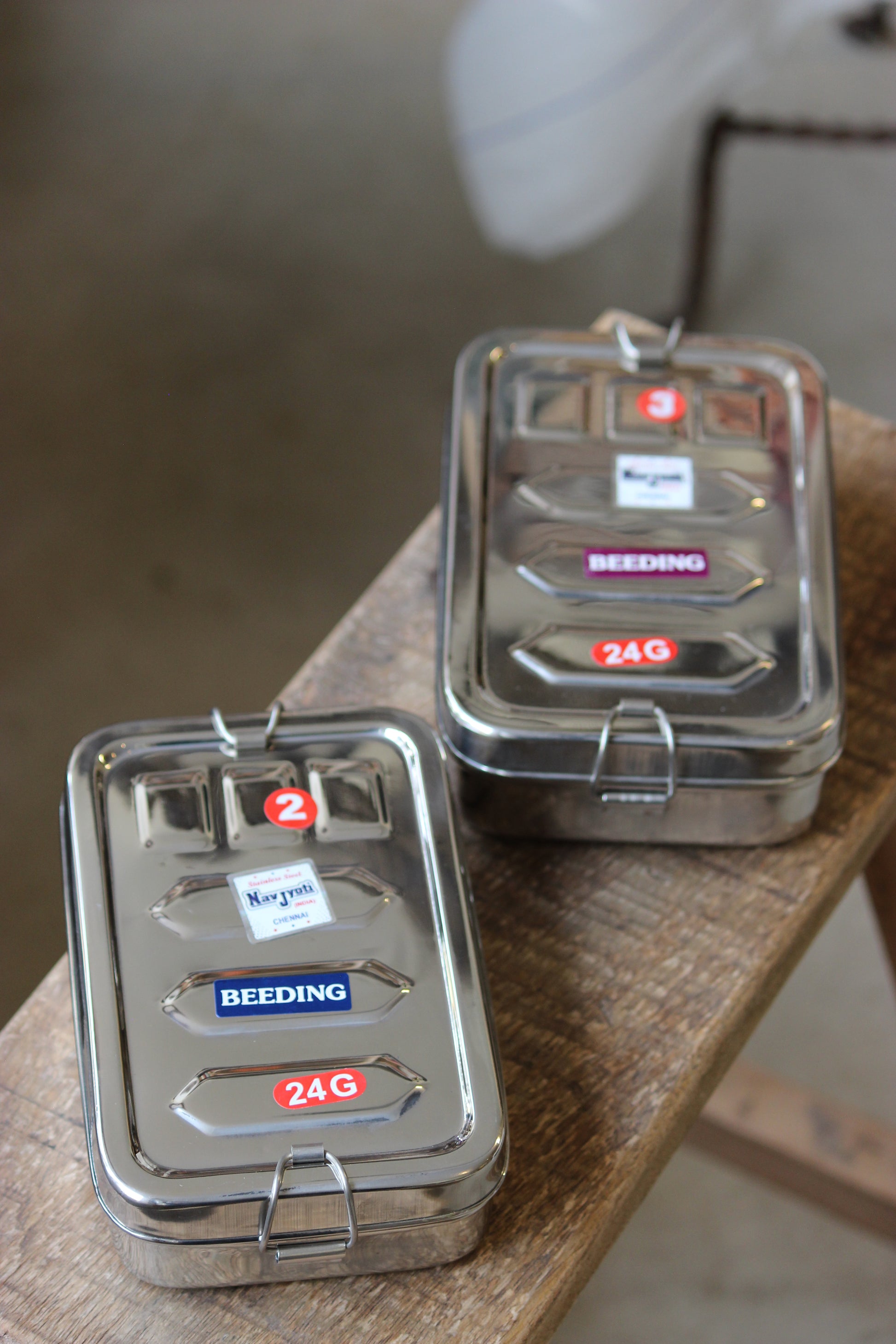 Two metallic tackle boxes with brand labels on a wooden surface.