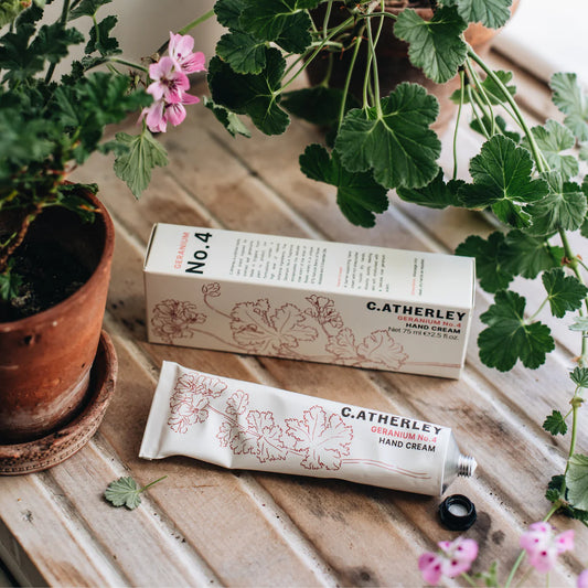 C. Atherley hand cream No.4 Attar of Roses pelargonium scent and packaging on a wooden surface with plants and flowers.