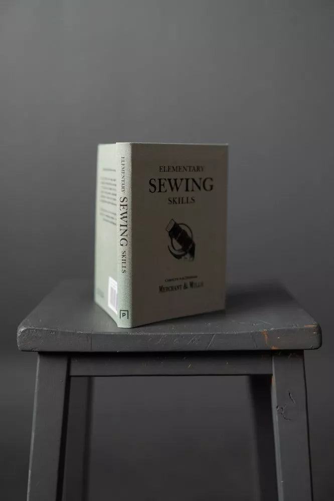 Book titled 'Elementary Sewing Skills' on a dark surface with a gray background