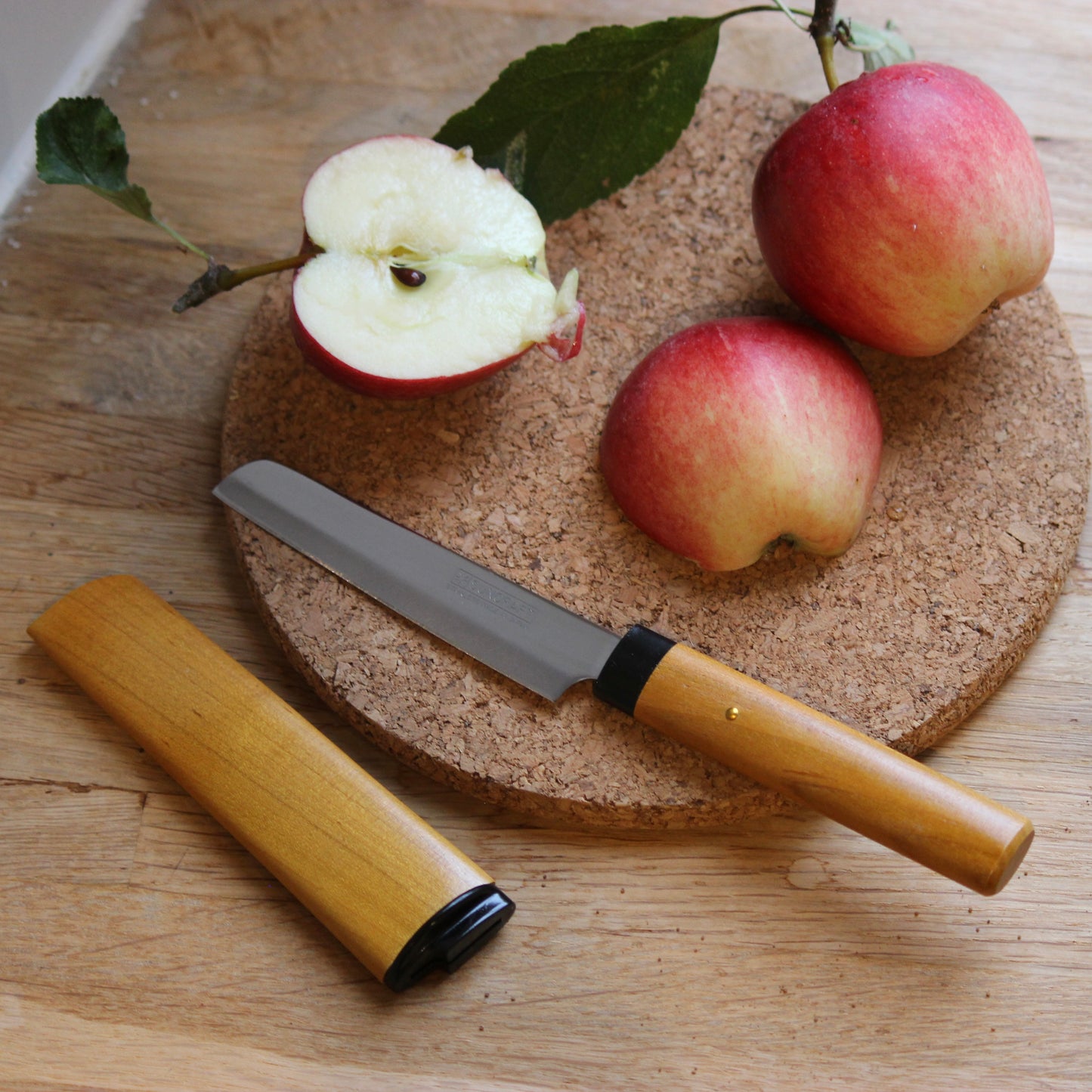 Apple, knife, and cork board on a wooden surface