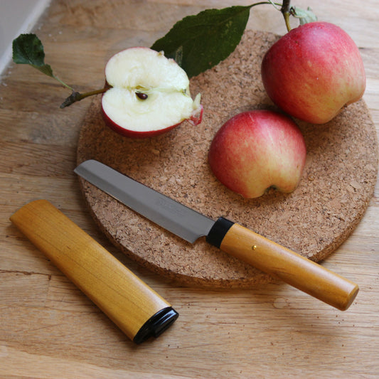 Apple, knife, and cork board on a wooden surface