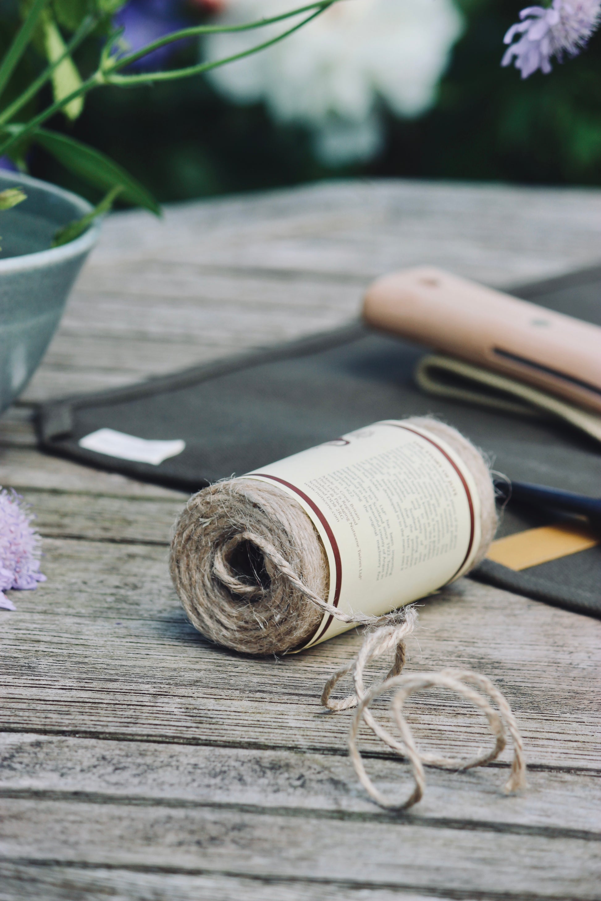 Roll of twine on a wooden surface with blurred flowers in the background