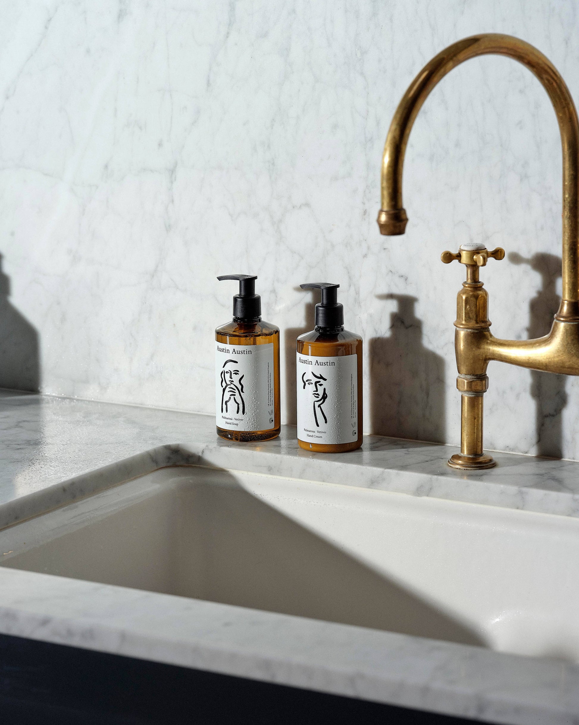 Two bottles of Austin Austin soap on a marble countertop with a gold faucet.