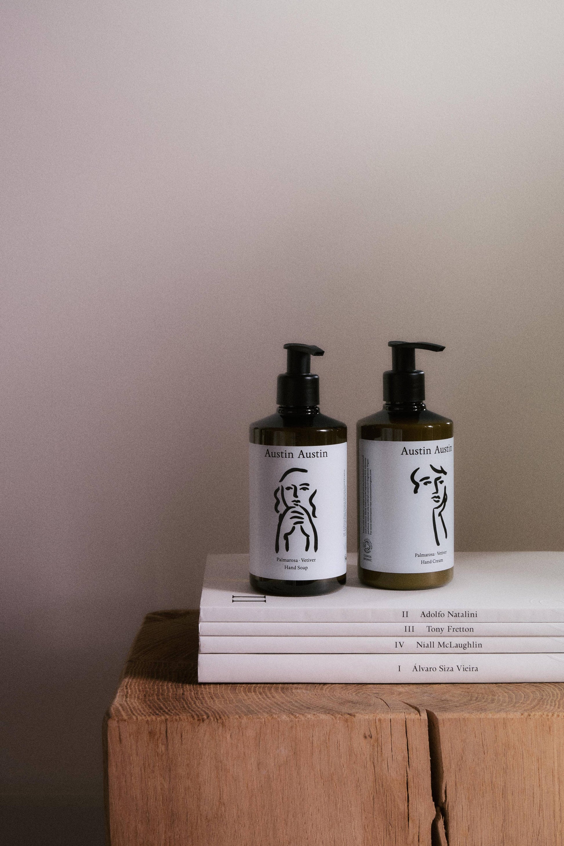 Two bottles with black pump dispensers on a stack of books against a plain wall.