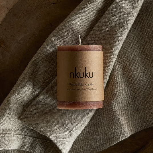 Candle with 'nkuku' branding on a wooden surface with a cloth