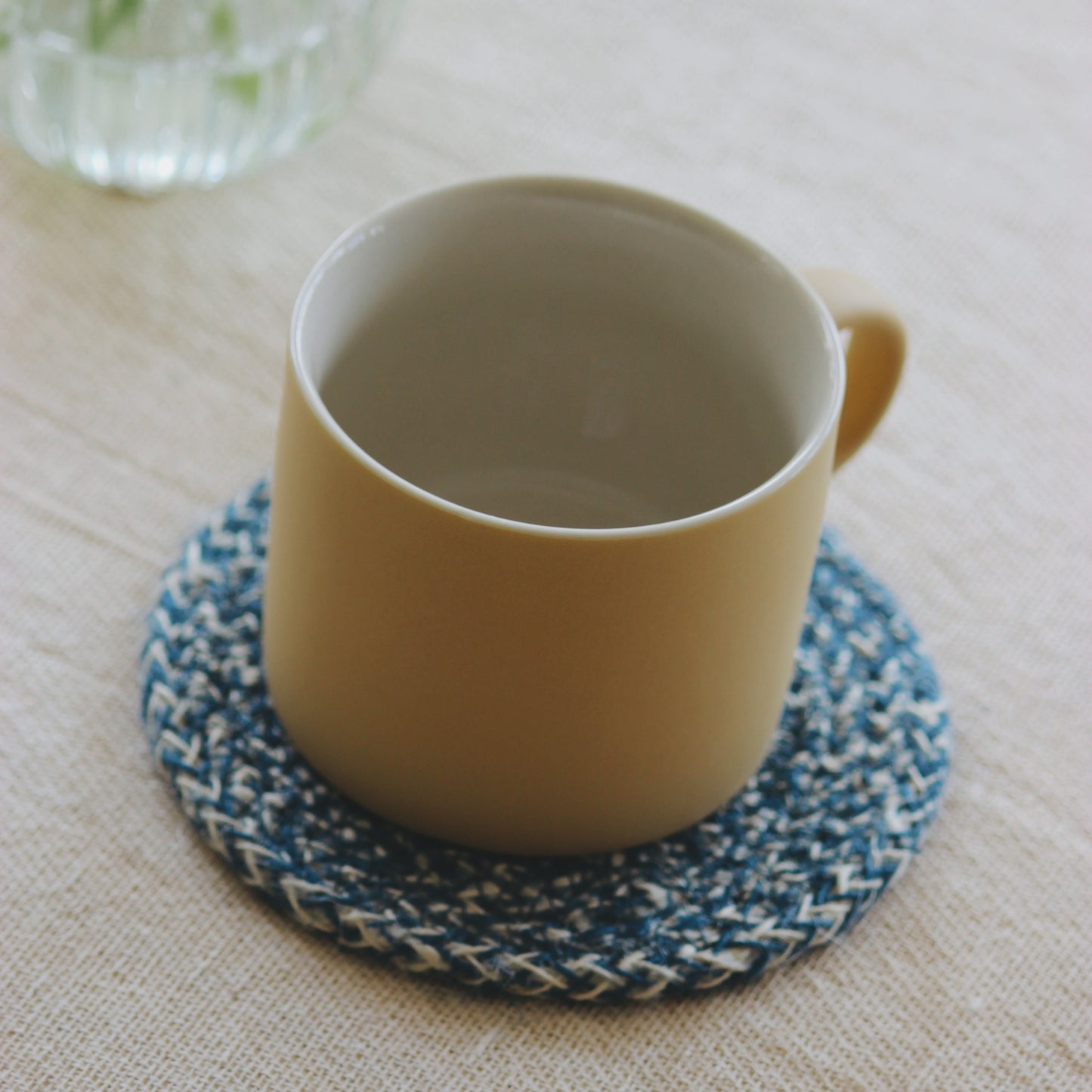 Yellow mug on a blue woven coaster with a glass vase in the background