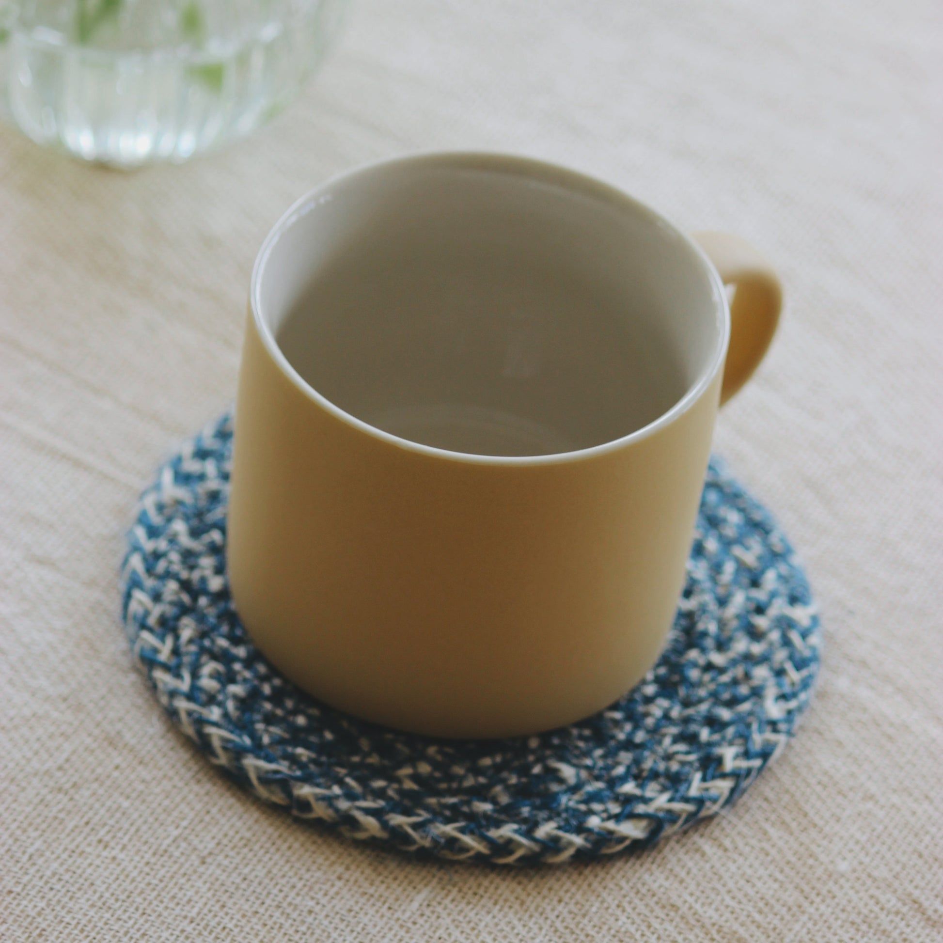 Yellow mug on a blue woven coaster with a glass vase in the background