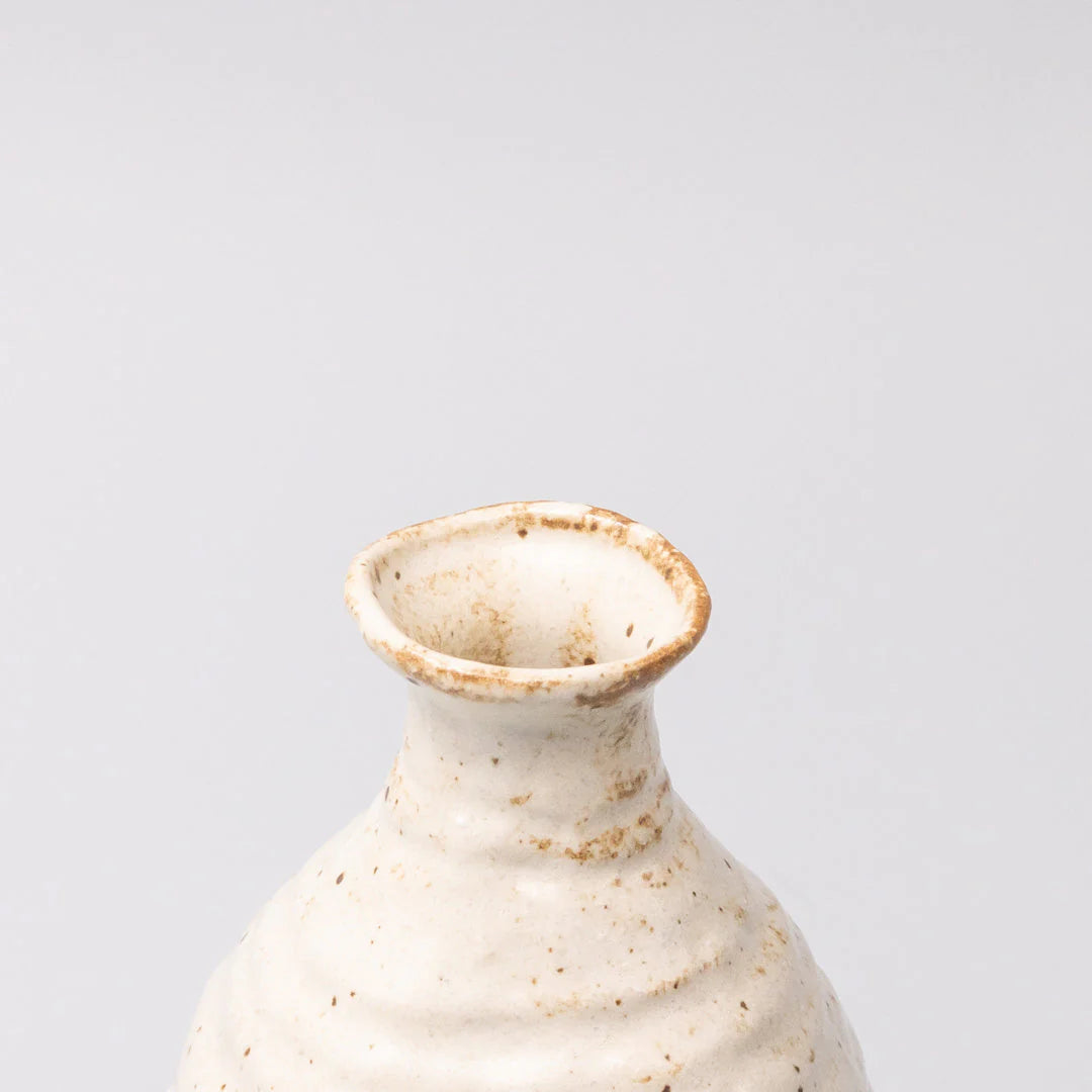 White ceramic vase with brown speckles on a light gray background