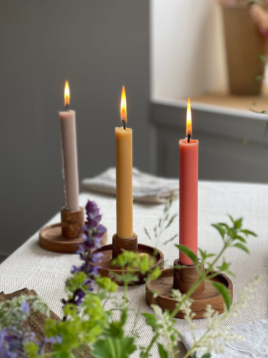 Three pastel coloured and neutral plant-based dinner candles in wooden candle holders styled on a dining table