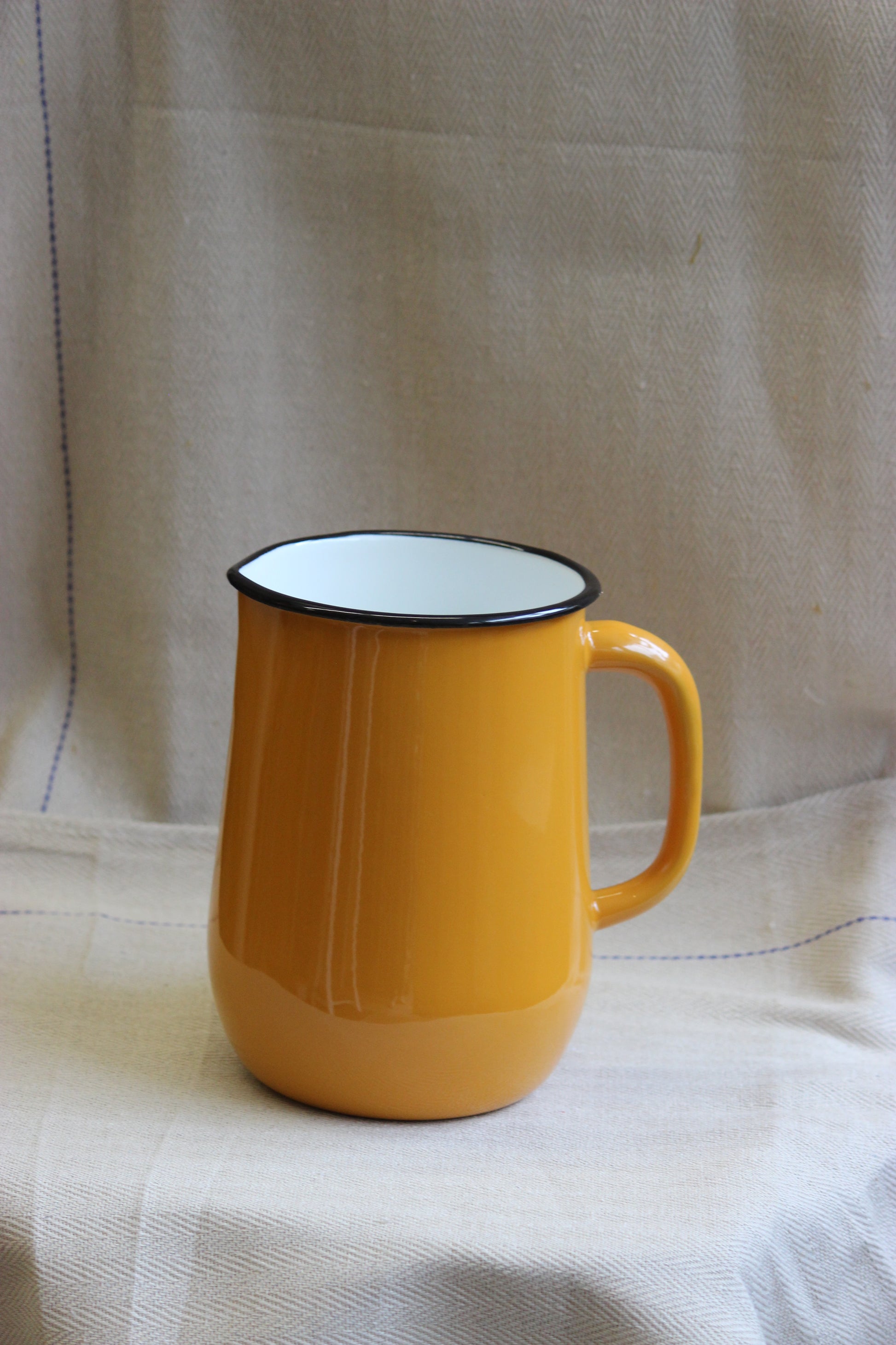 Yellow jug with a white interior on a beige fabric background