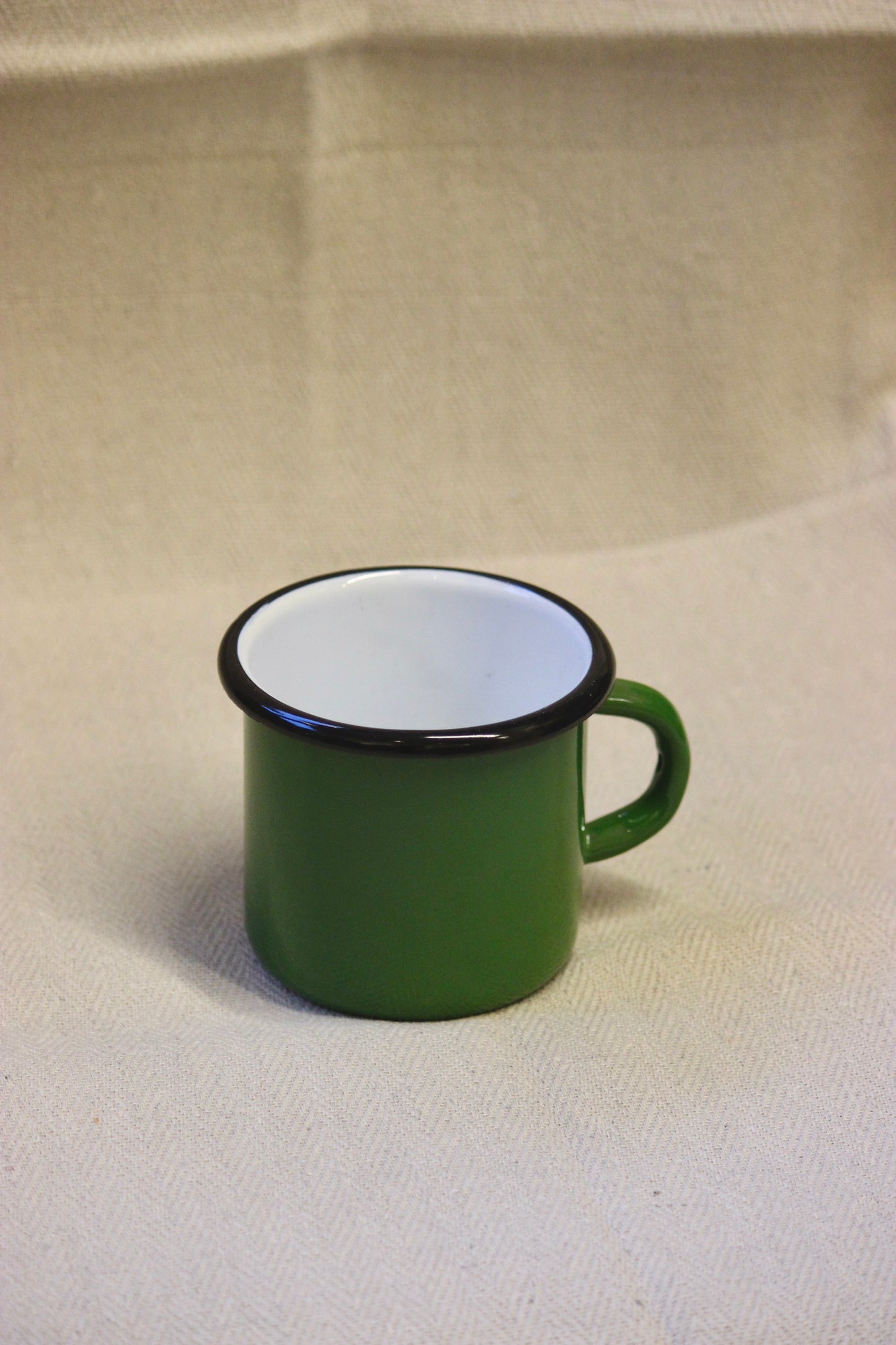 Green enamel mug with black rim on a beige background