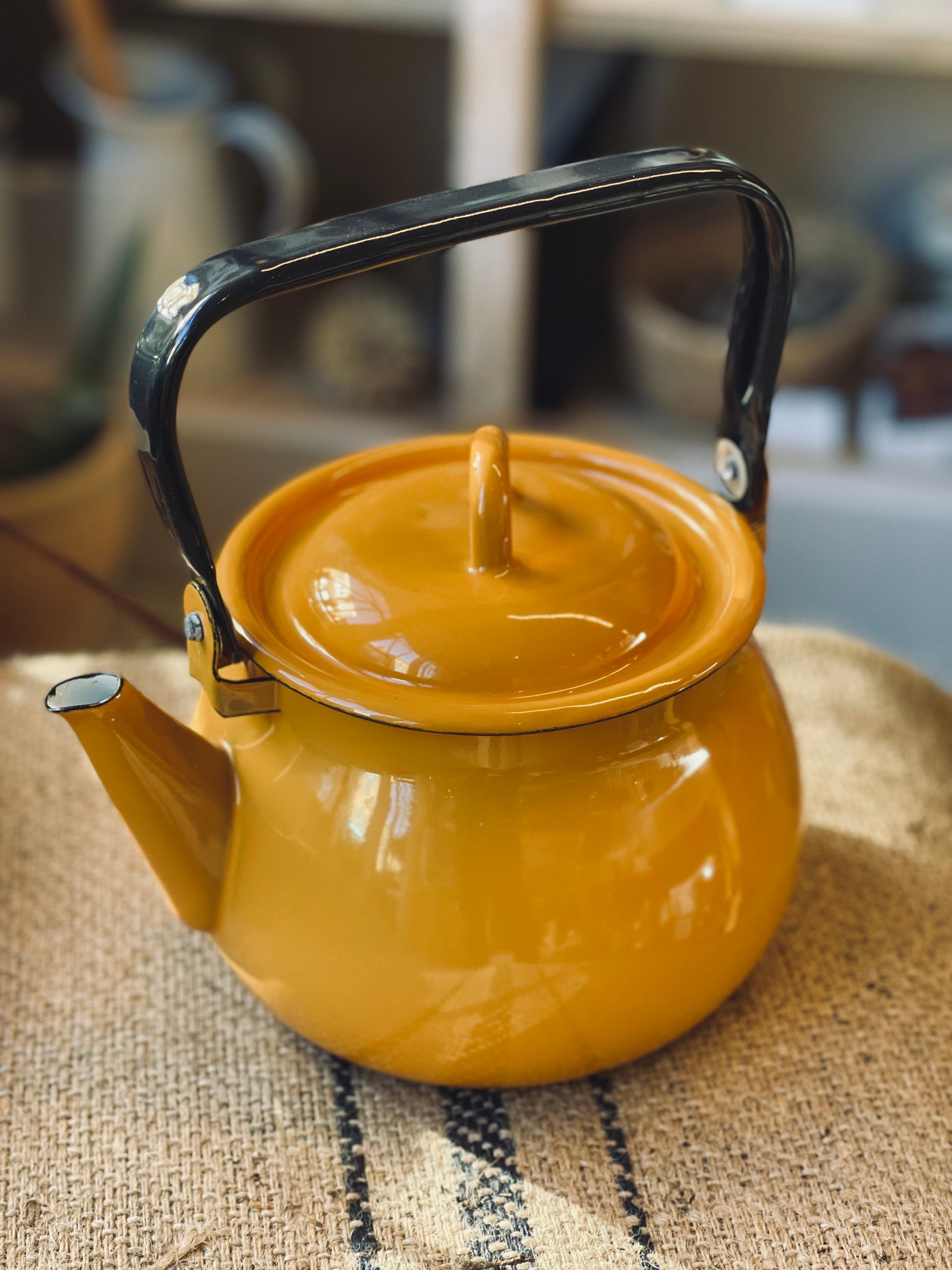 Yellow ukraine made enamel kettle with black handle on a textured surface