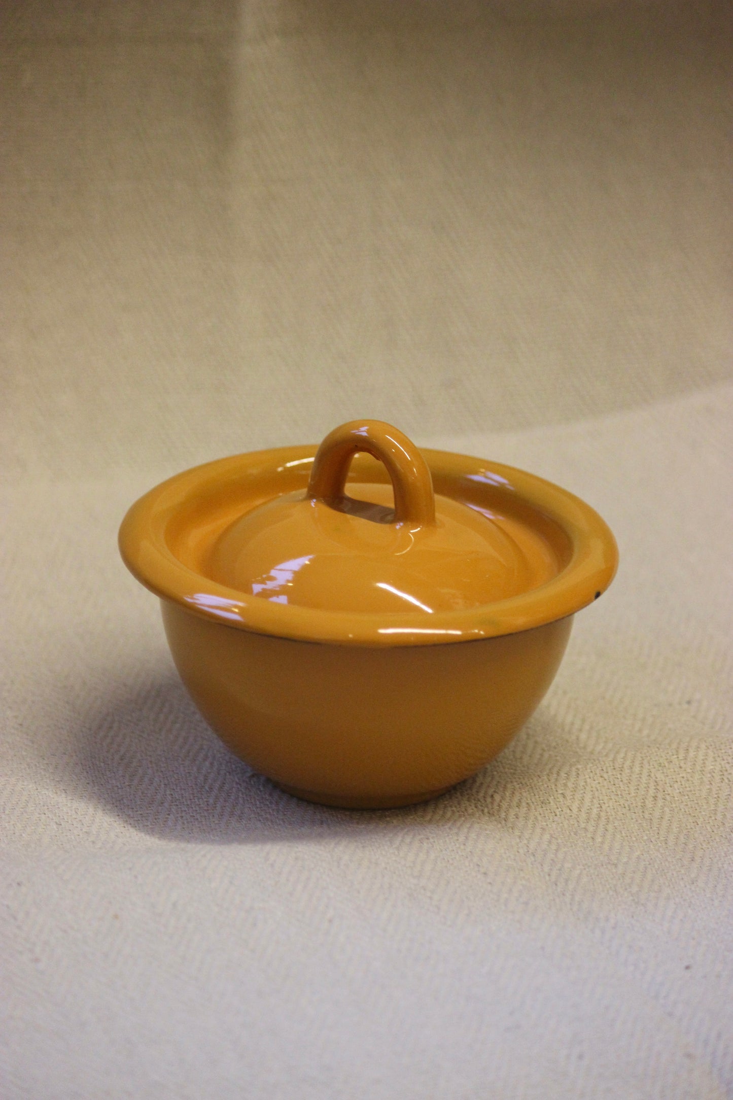 Small yellow ceramic pot with a lid on a beige background