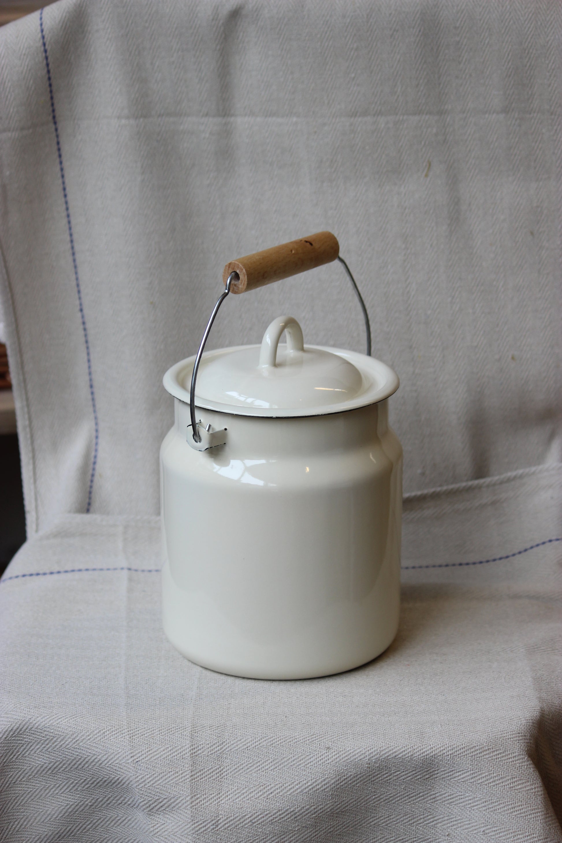 White enamel jar with a wooden handle on a light fabric background