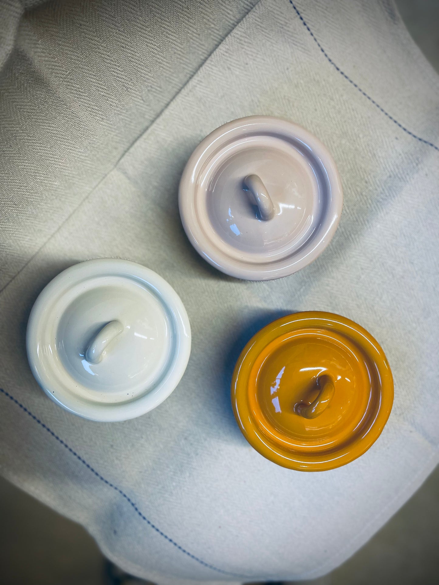 Three ceramic bowl with lids of different colours on a textured surface