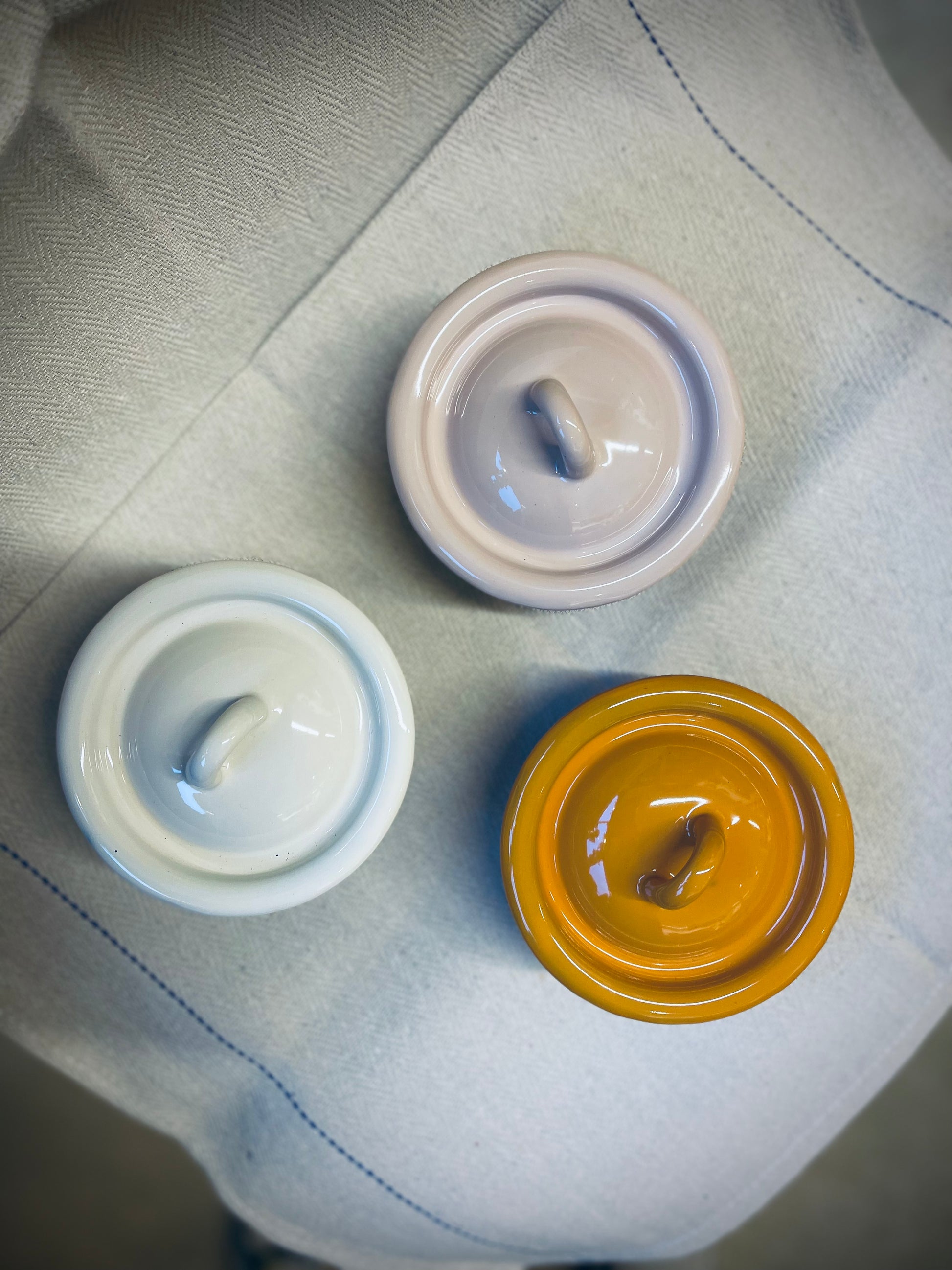 Three ceramic bowl with lids of different colours on a textured surface