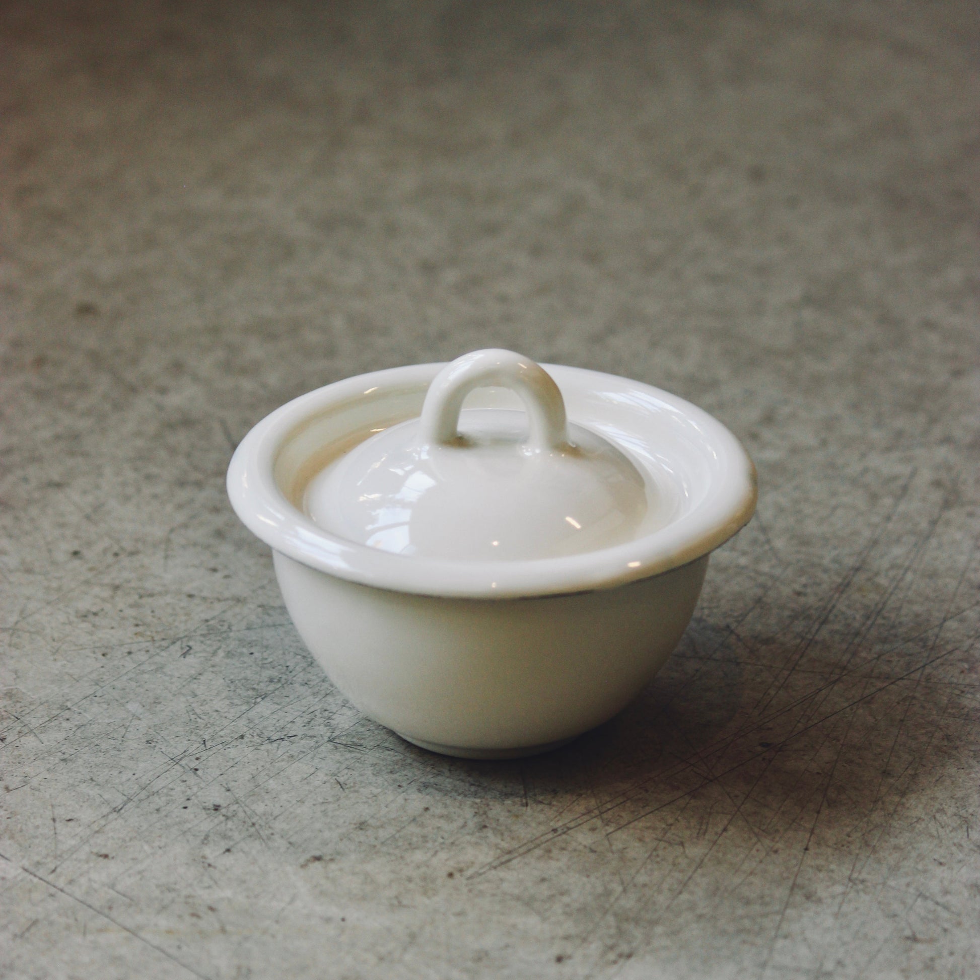 White enamel bowl with lid on a textured surface