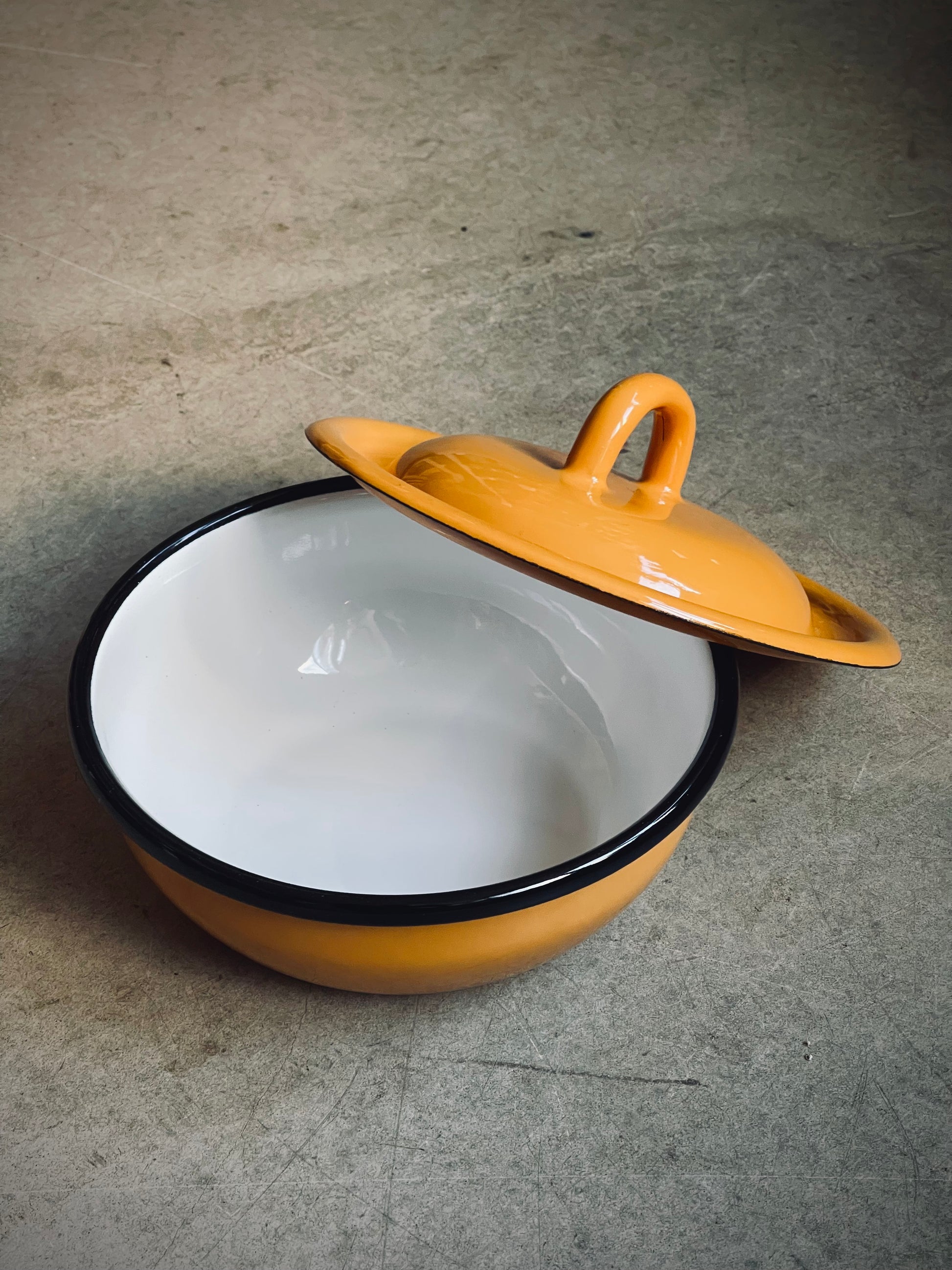 Yellow enameled enamel pot with a white interior on a gray surface
