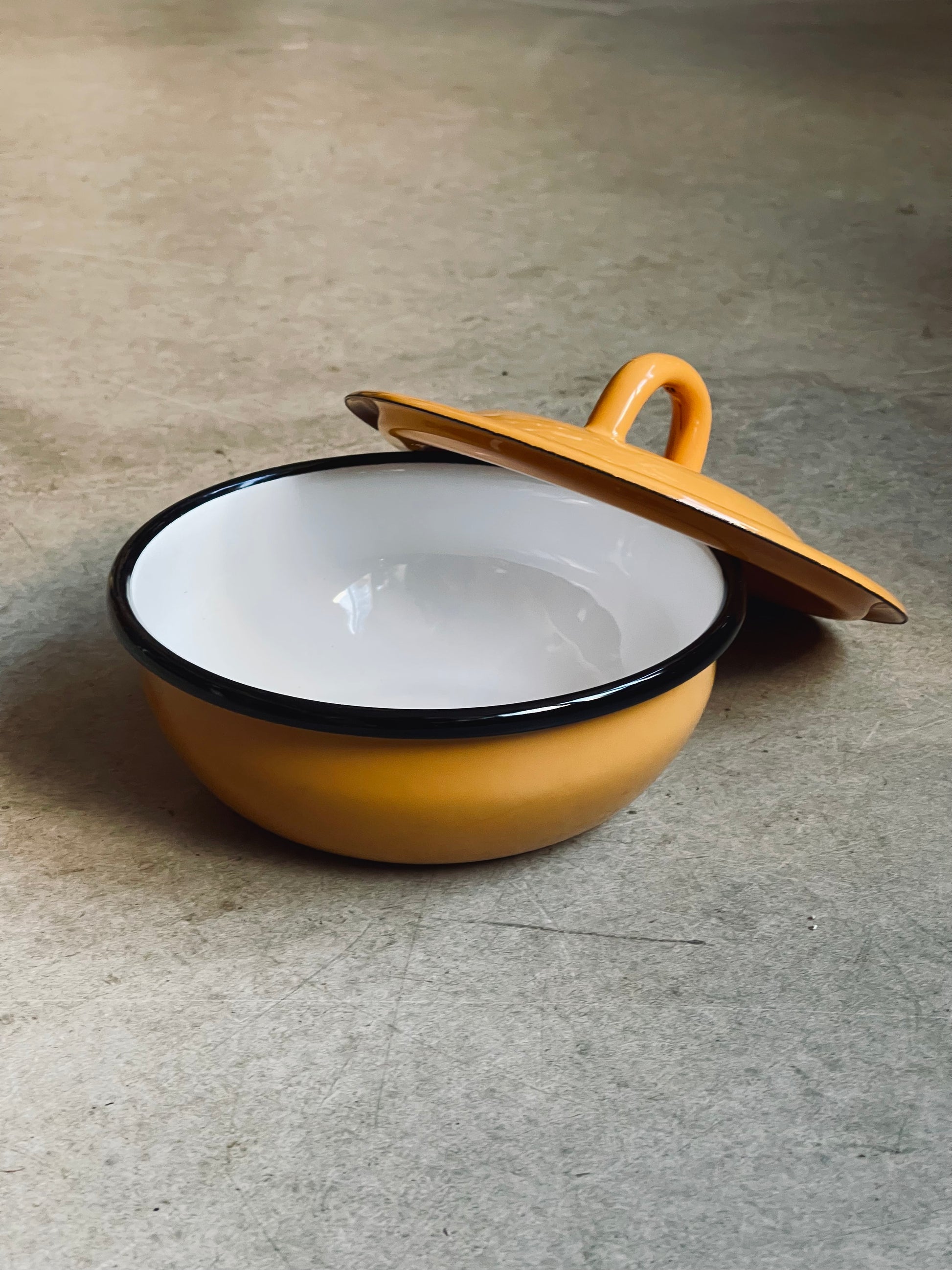 Yellow enameled pot with a wooden lid on a gray surface