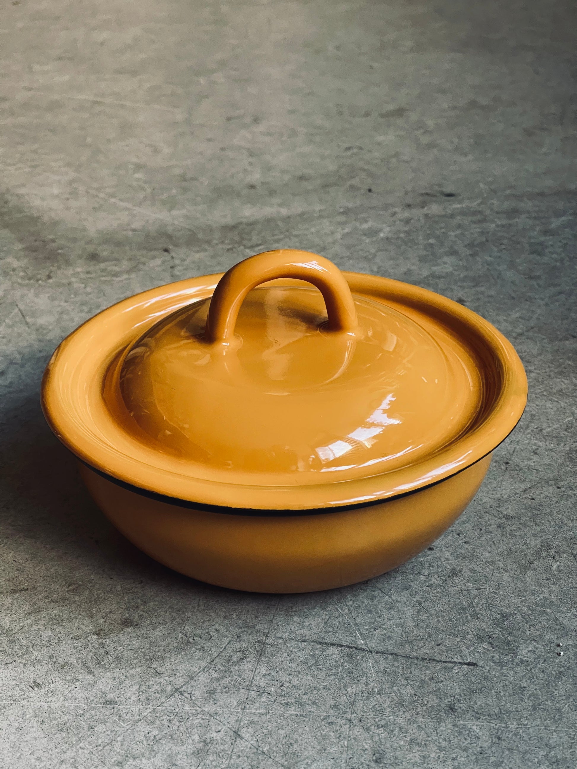 Yellow enamel pot with lid on a grey surface