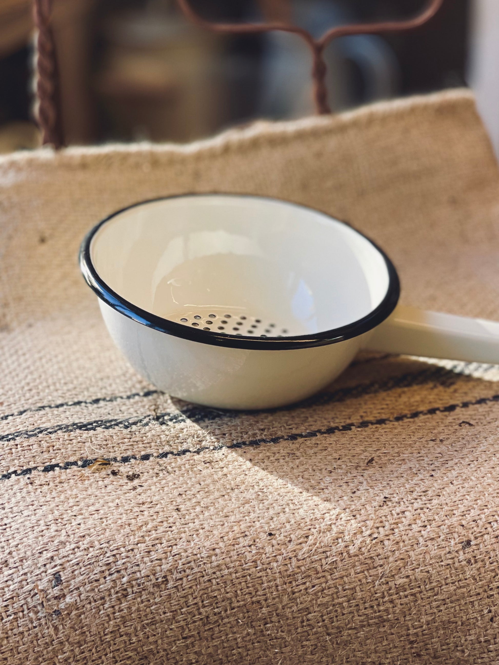 Cream Ukrainian Enamelware Colander with black rim on a textured fabric surface