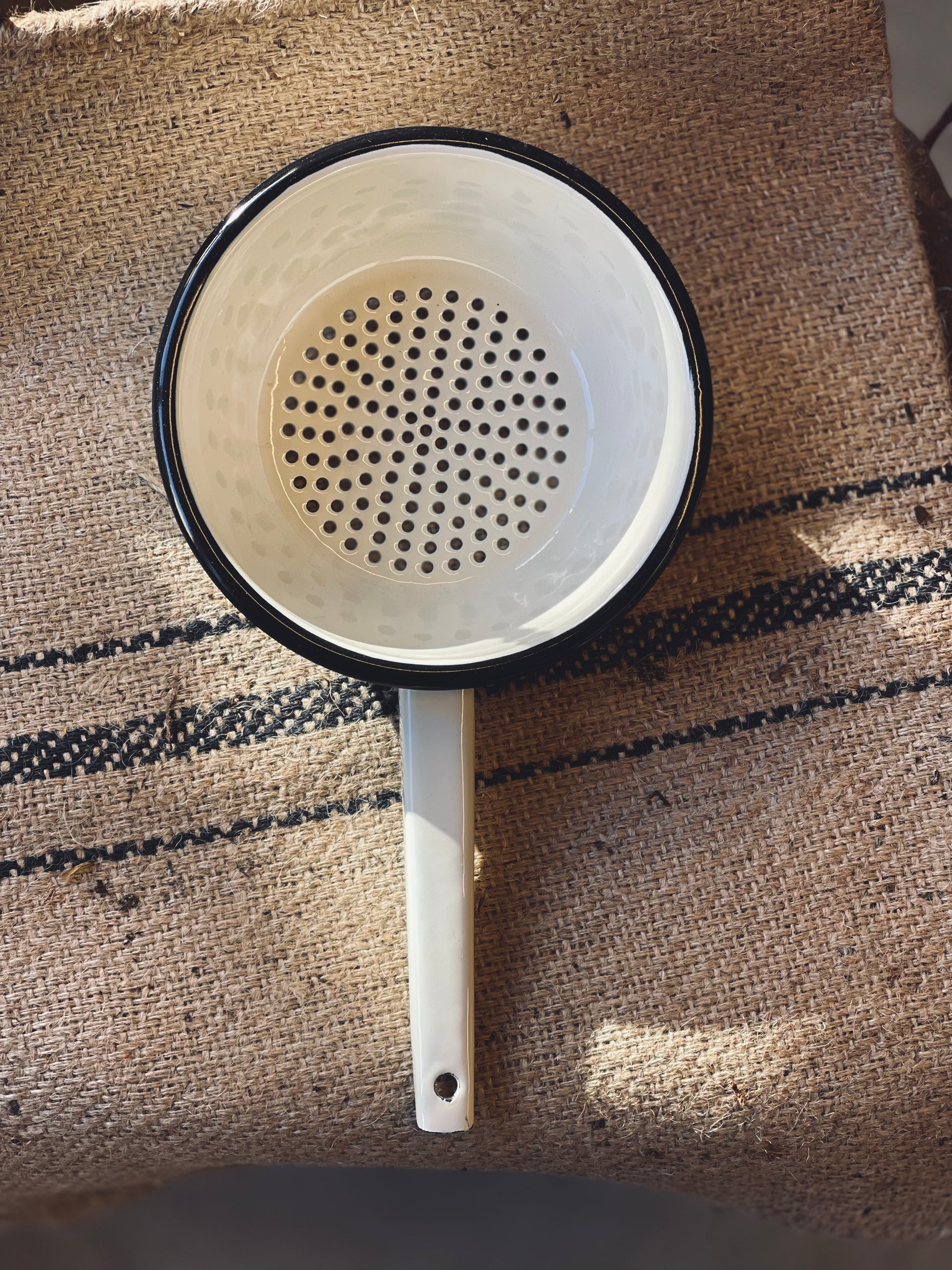 White colander with black rim on a textured fabric background