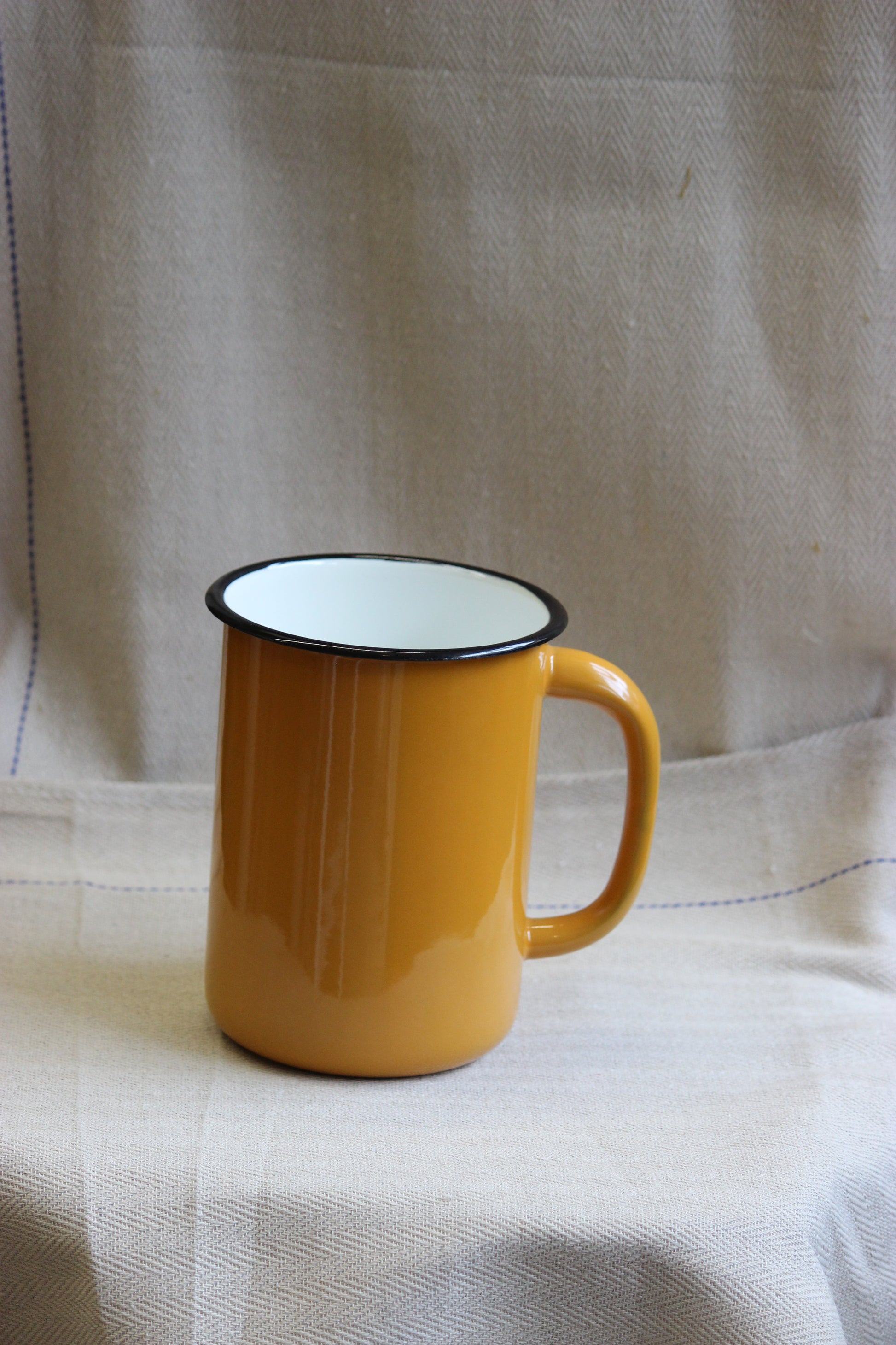 Yellow enamel jug with a white rim on a checkered fabric background