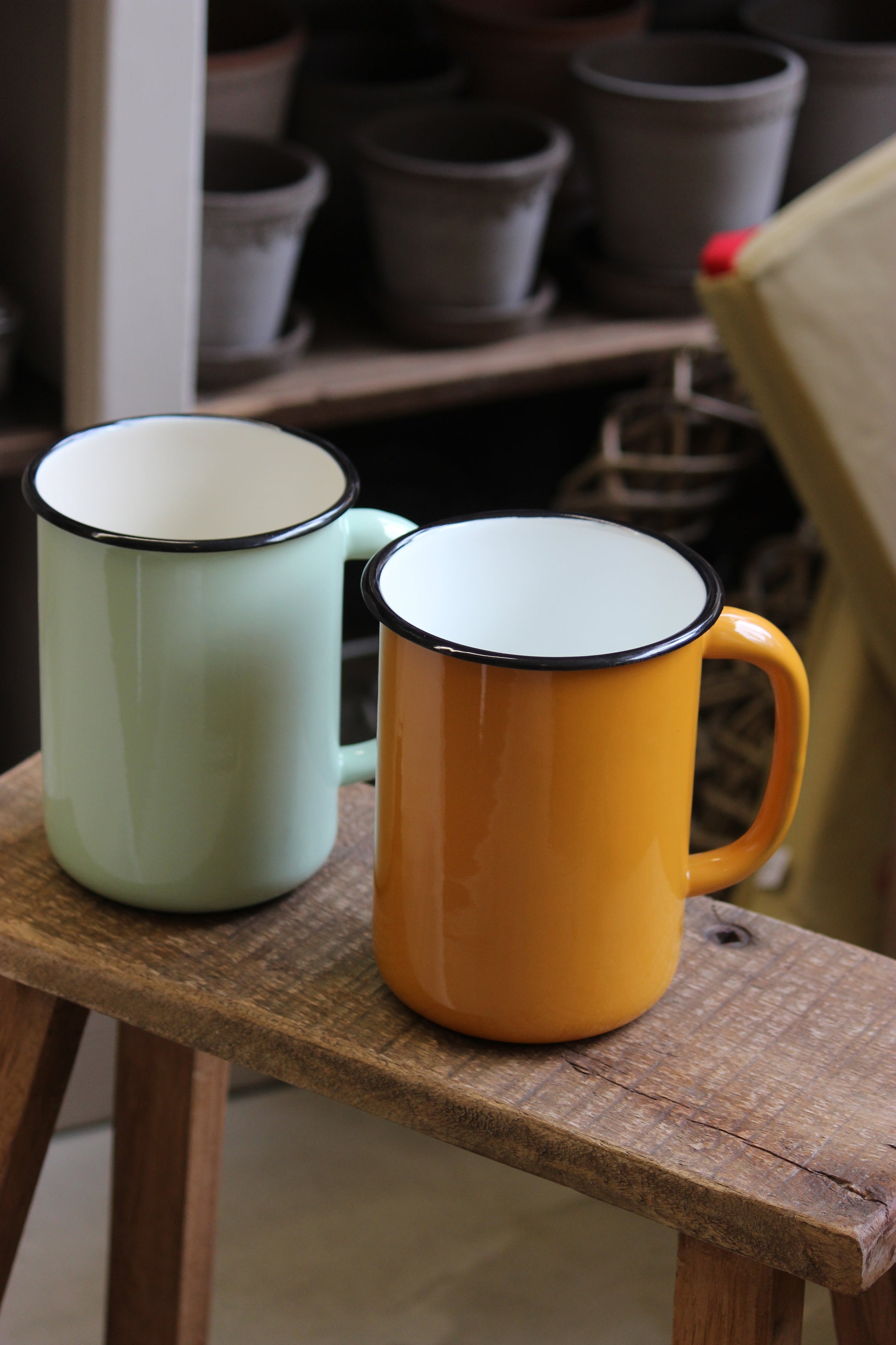 Two enamel jugs, one yellow and one green, hanging on a wooden rack.