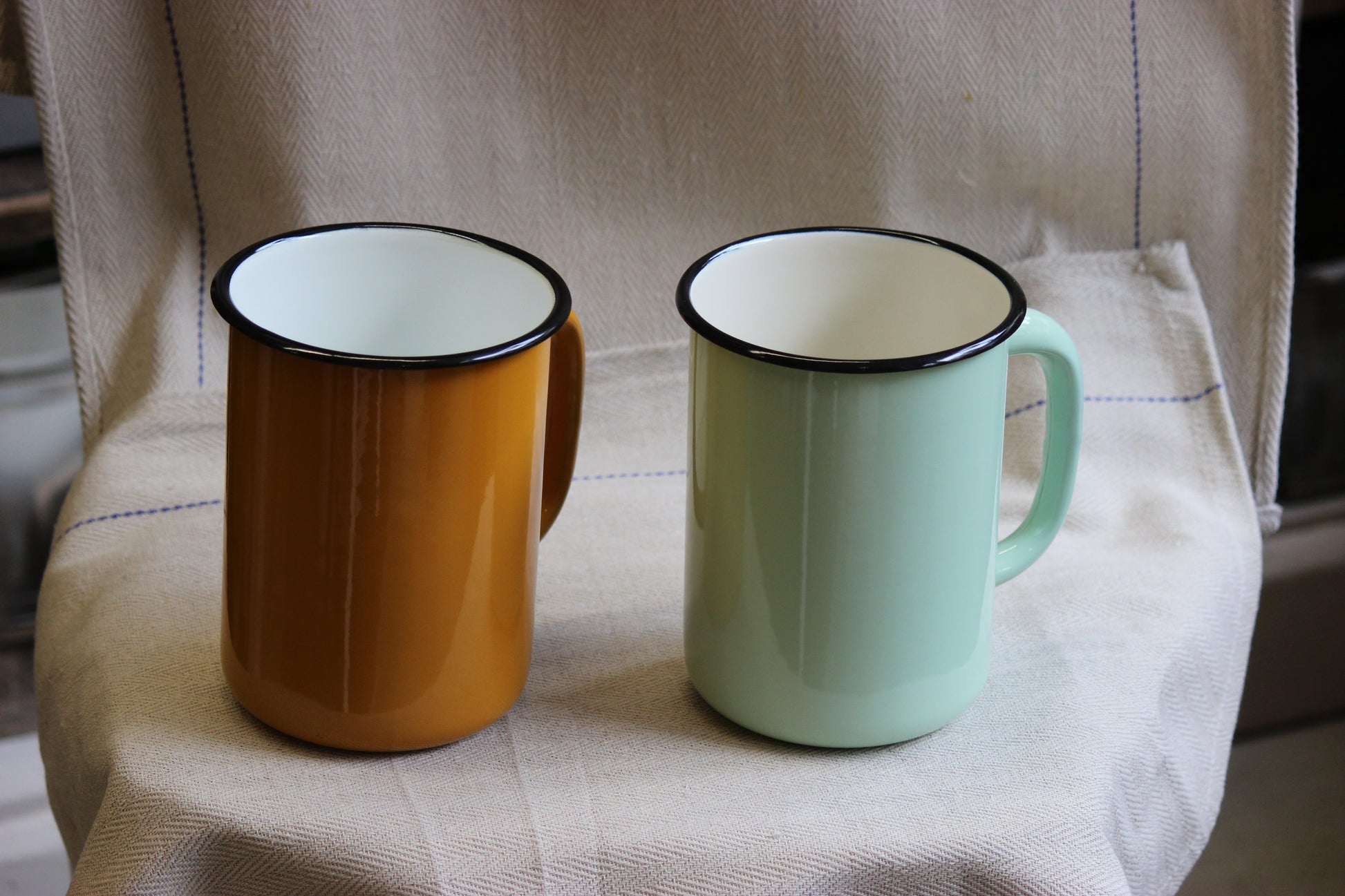 Two enamel jugs, one mustard yellow and one green, on a textured surface.