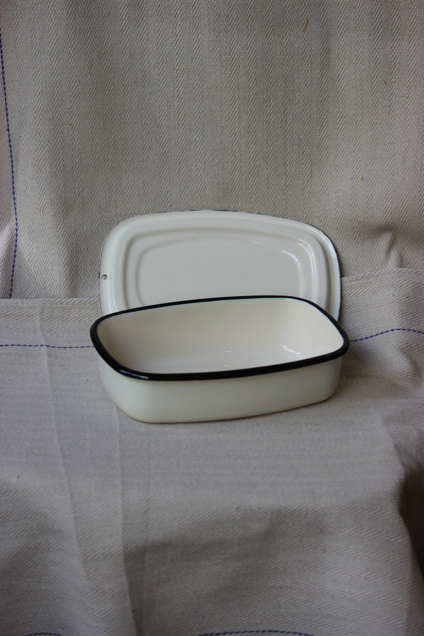 White Ukrainian Enamel Storage Casserole Dish (Cream) with black rim on a beige fabric background