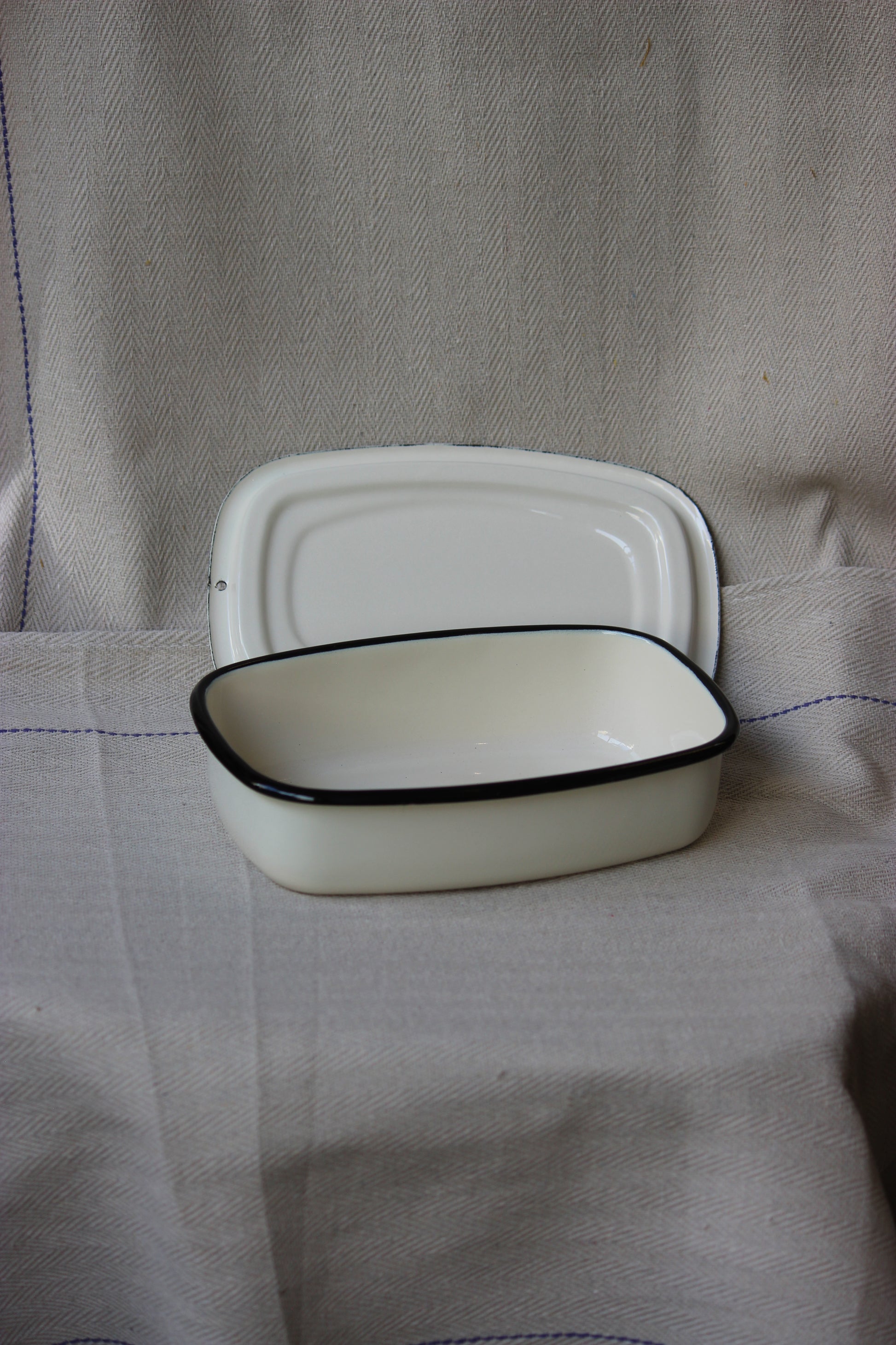 White Ukrainian Enamel Storage Casserole Dish (Cream) with black rim on a beige fabric background