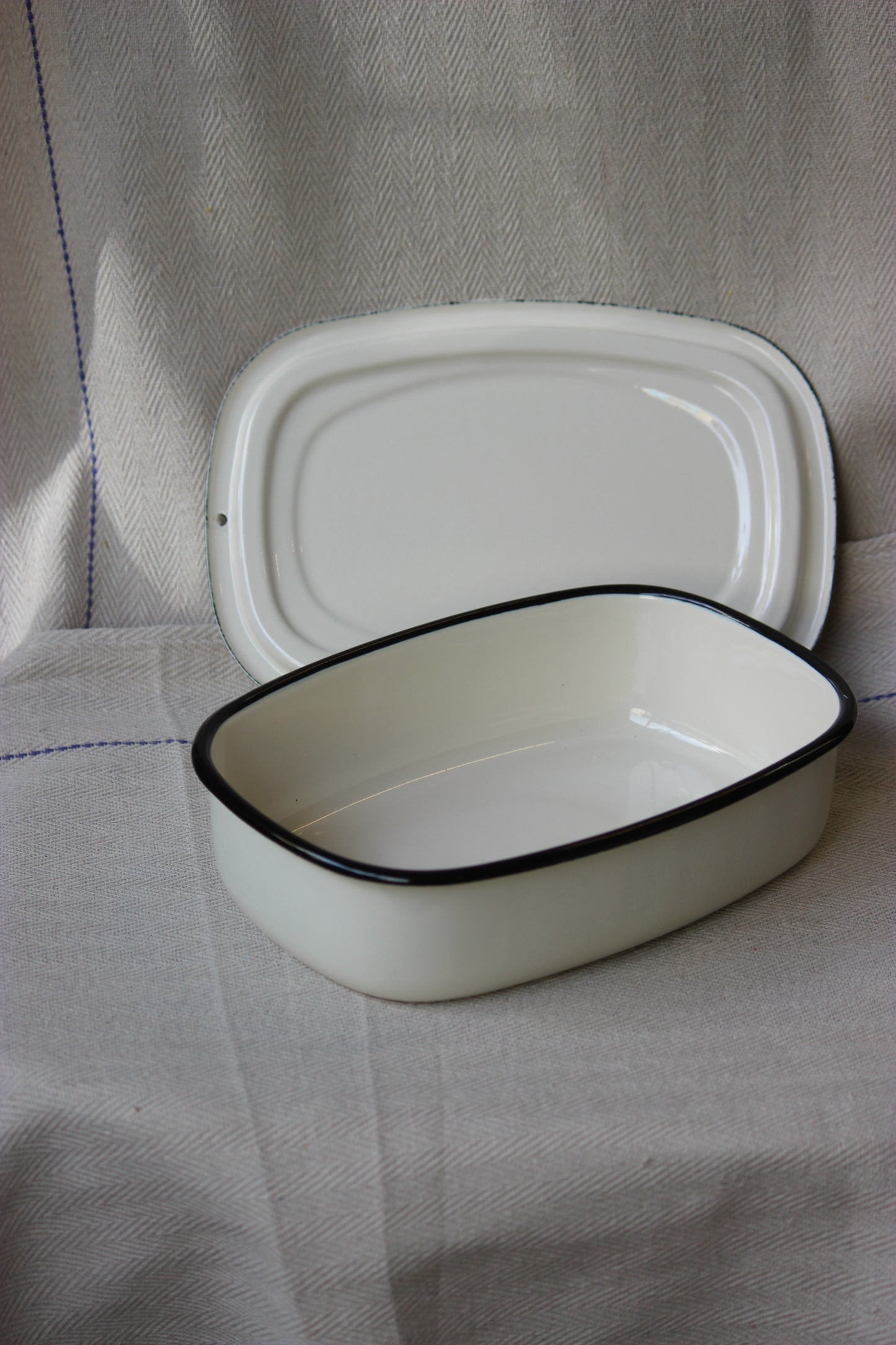 White enamel cooking dishes with black rim on a textured surface