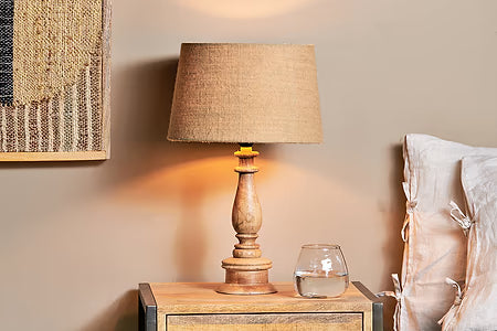 Mango Wood lamp on a nightstand with a glass of water and decorative pillows in the background.