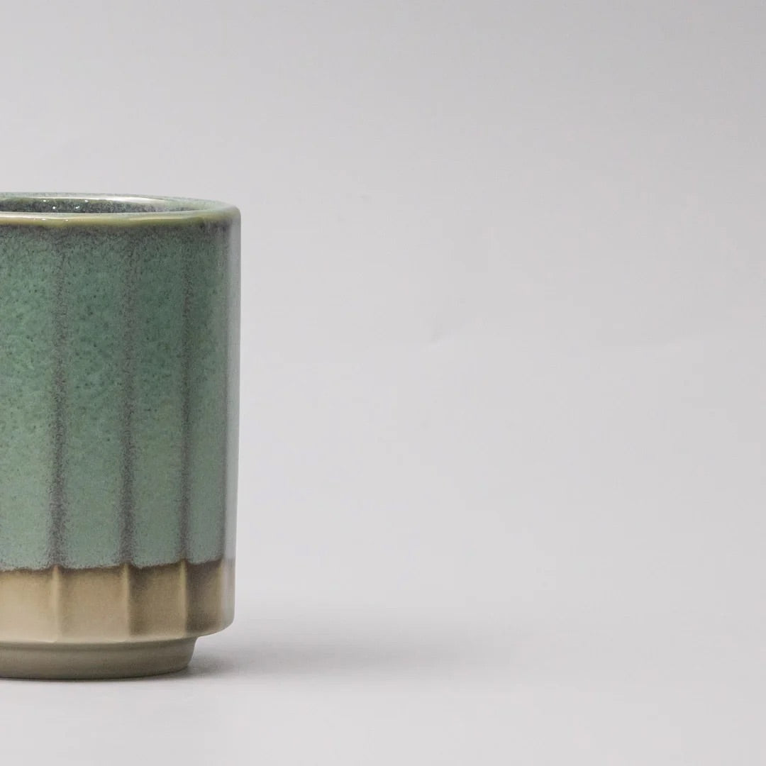 A close-up of a ceramic cup or small vase with a fluted rim, featuring a speckled sage green glaze on the upper portion and a matte beige base on a light gray background. Vintage Mint Mug Omomi Made in Japan 