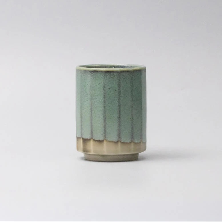 A small ceramic cup with a fluted exterior, featuring a sage green glaze on the upper portion and a natural beige clay finish on the lower portion, set against a plain light gray background. Vintage Mint Mug Omomi Made in Japan 