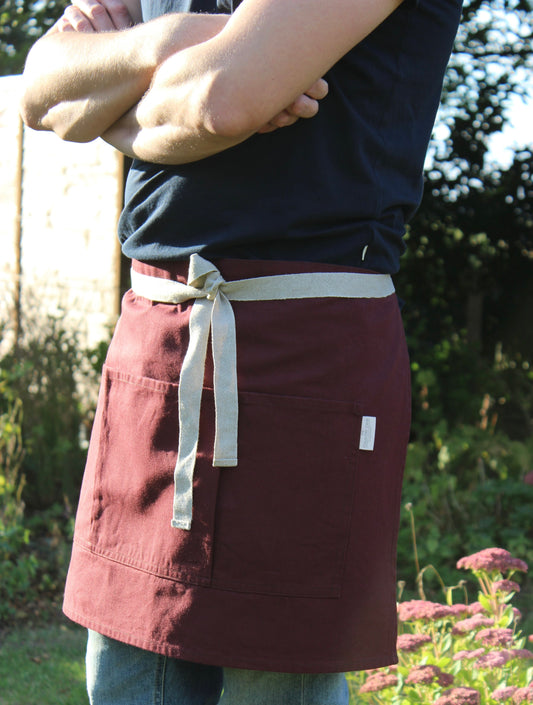 Person wearing a maroon apron with a white strap in an outdoor setting