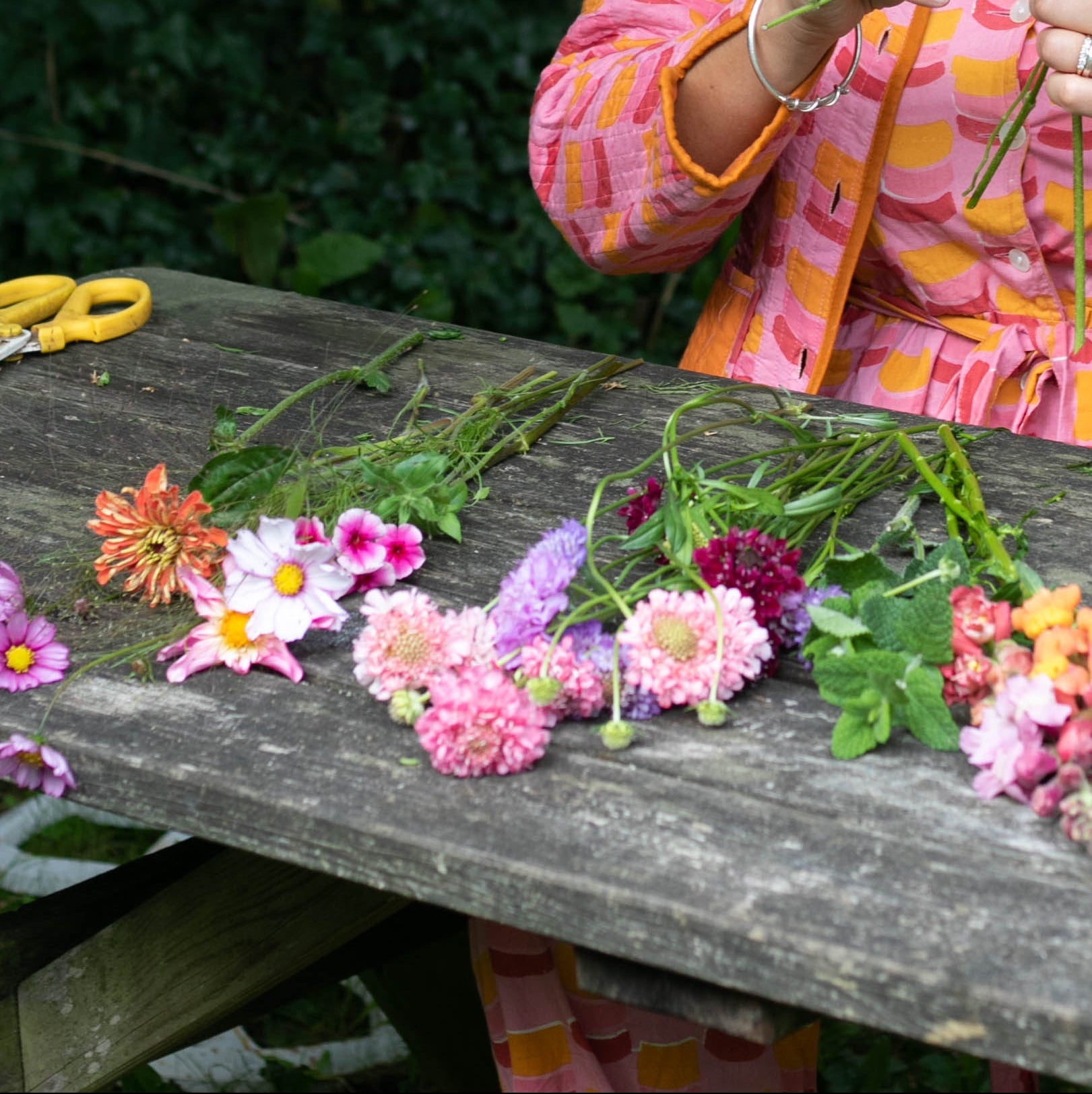 Person arranging flowers on a wooden table outdoors