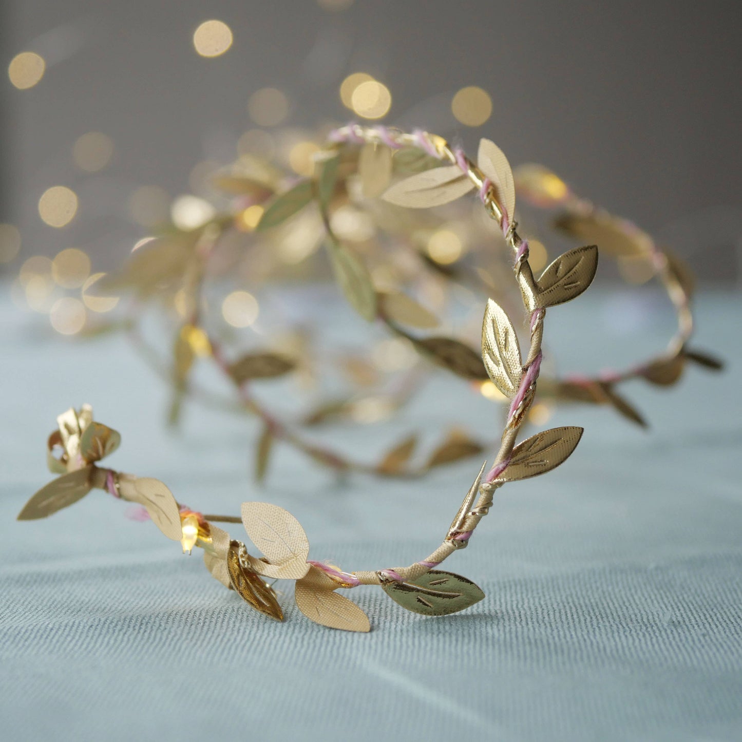 Gold leaf headband on a light blue fabric background with blurred lights in the background