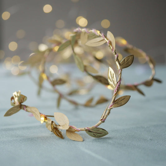 Gold leaf headband on a light blue fabric background with blurred lights in the background