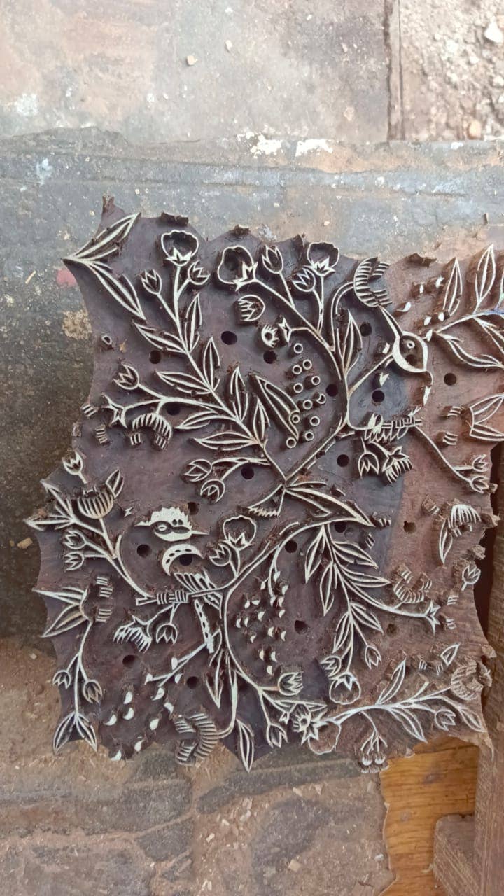 Decorative metal stamp with intricate floral design on a wooden block.