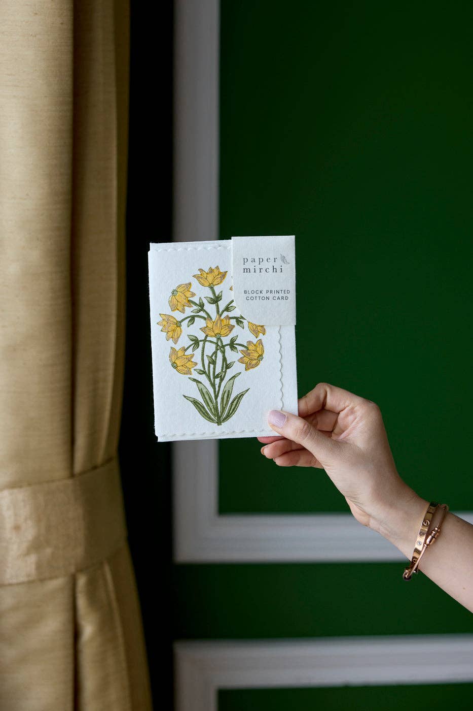 Hand holding a card with floral design against a green wall.