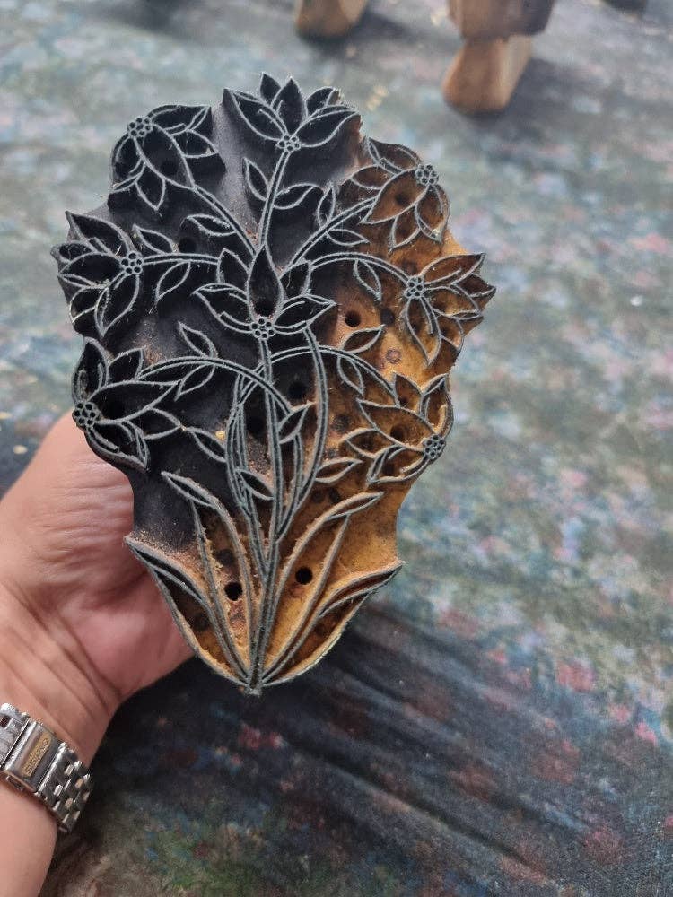 Decorative wooden printing block with floral design held by a hand on a textured surface.