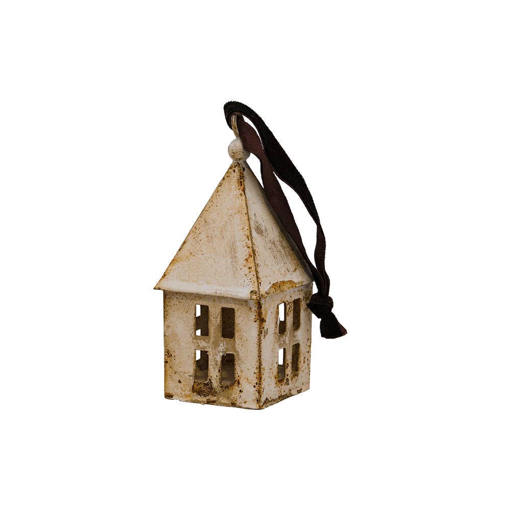 A small rustic metal house-shaped ornament with a distressed off-white finish, featuring cutout windows, a pointed roof, and a black hanging ribbon on a plain white background.