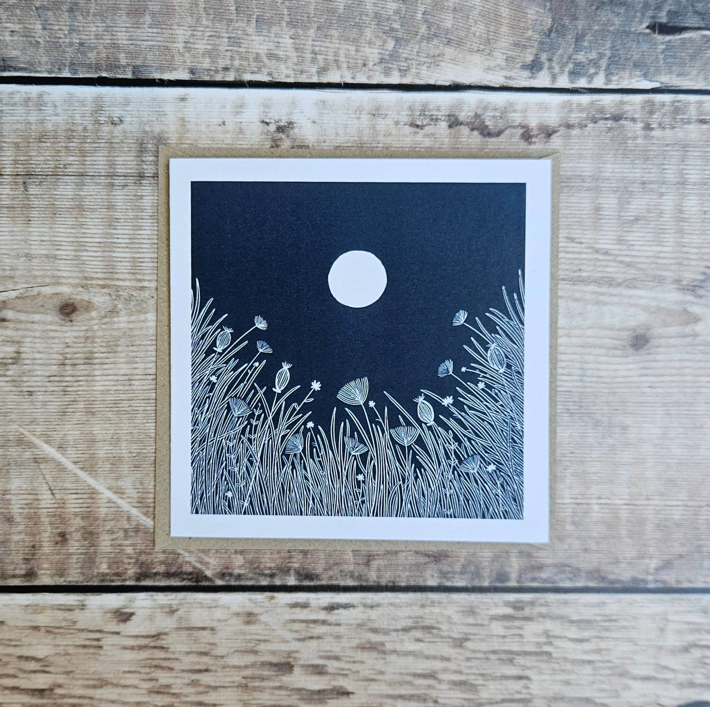 Card with a moon and grass design on a wooden surface